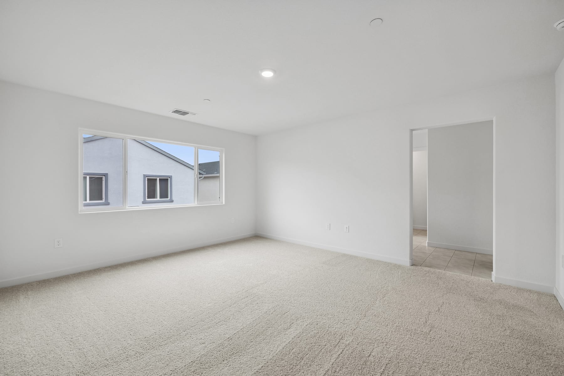 A spacious, minimalist room with a large window, hardwood flooring, and a doorway leading to another area.