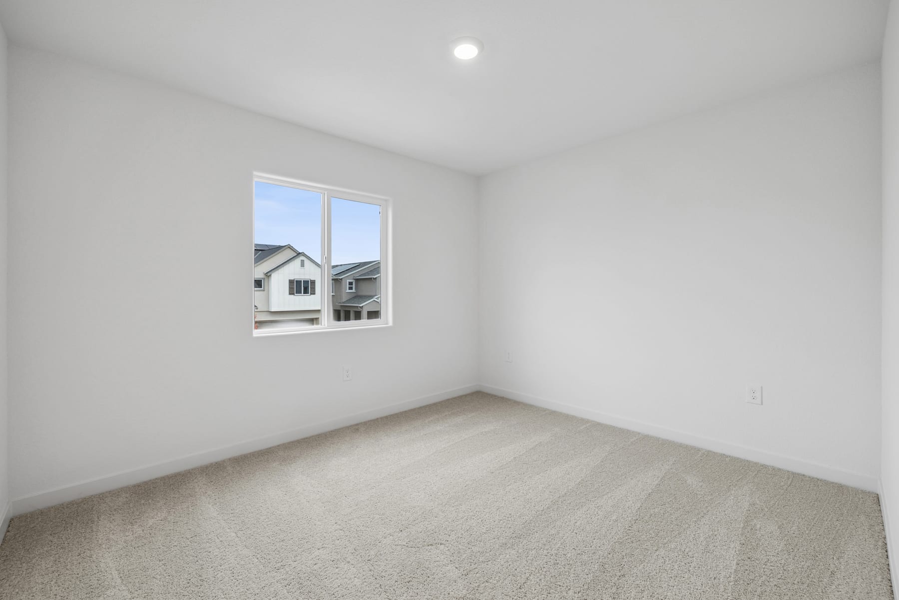 An empty, bright room with a window overlooking a residential neighborhood in the background.