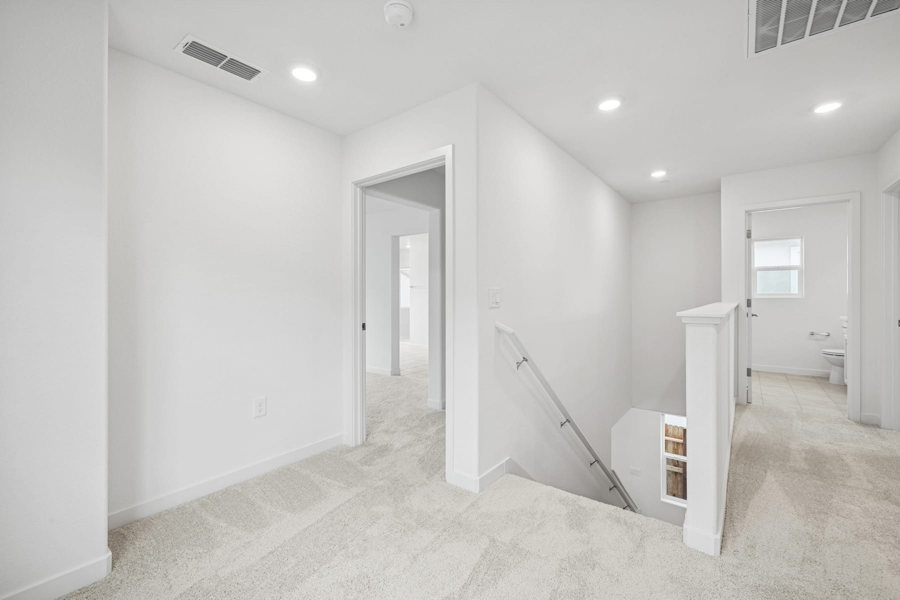 A bright, minimalist hallway with white walls, recessed lighting, and a partially open door leading to another room.
