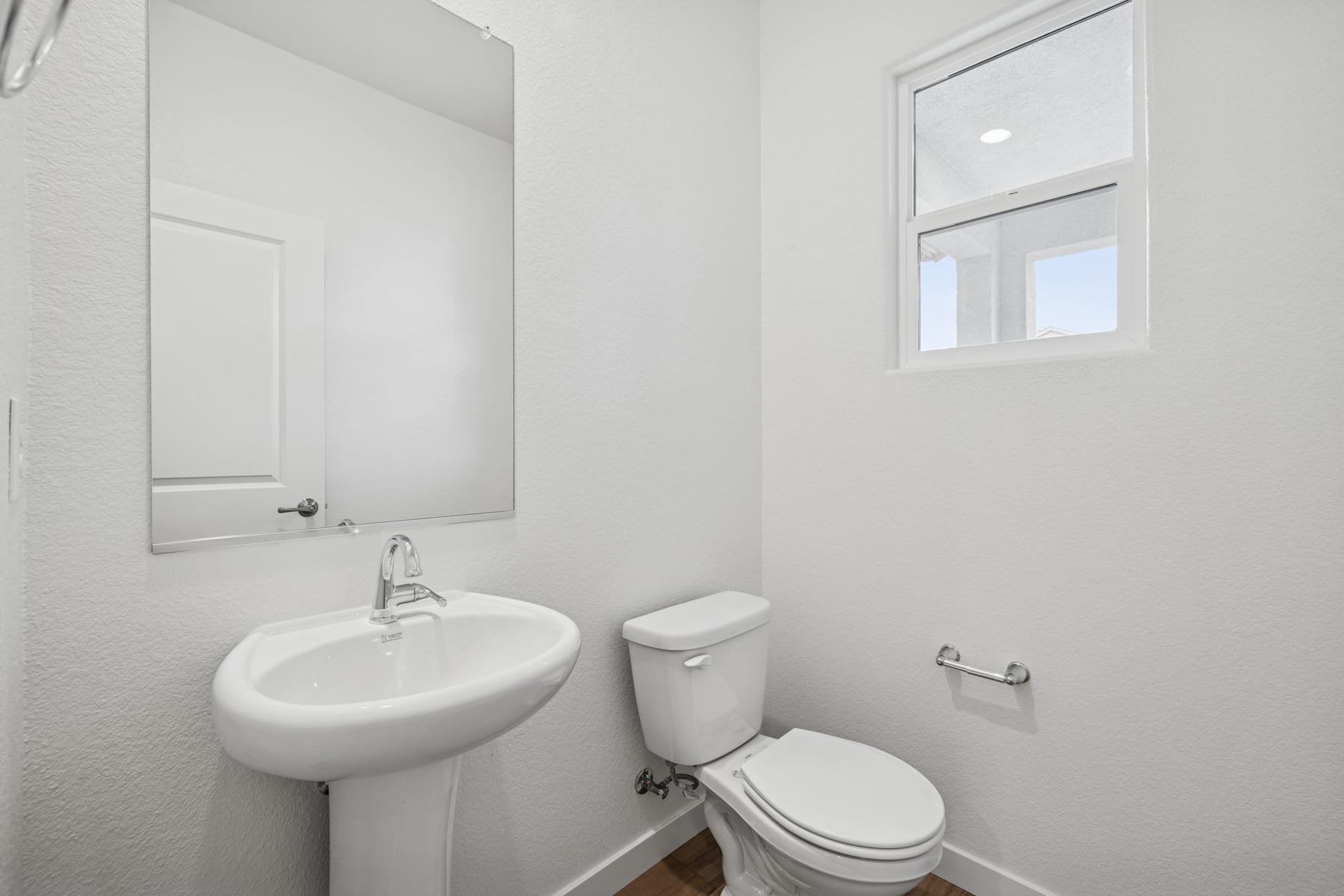 A simple, clean bathroom with a pedestal sink, toilet, and a window providing natural light.