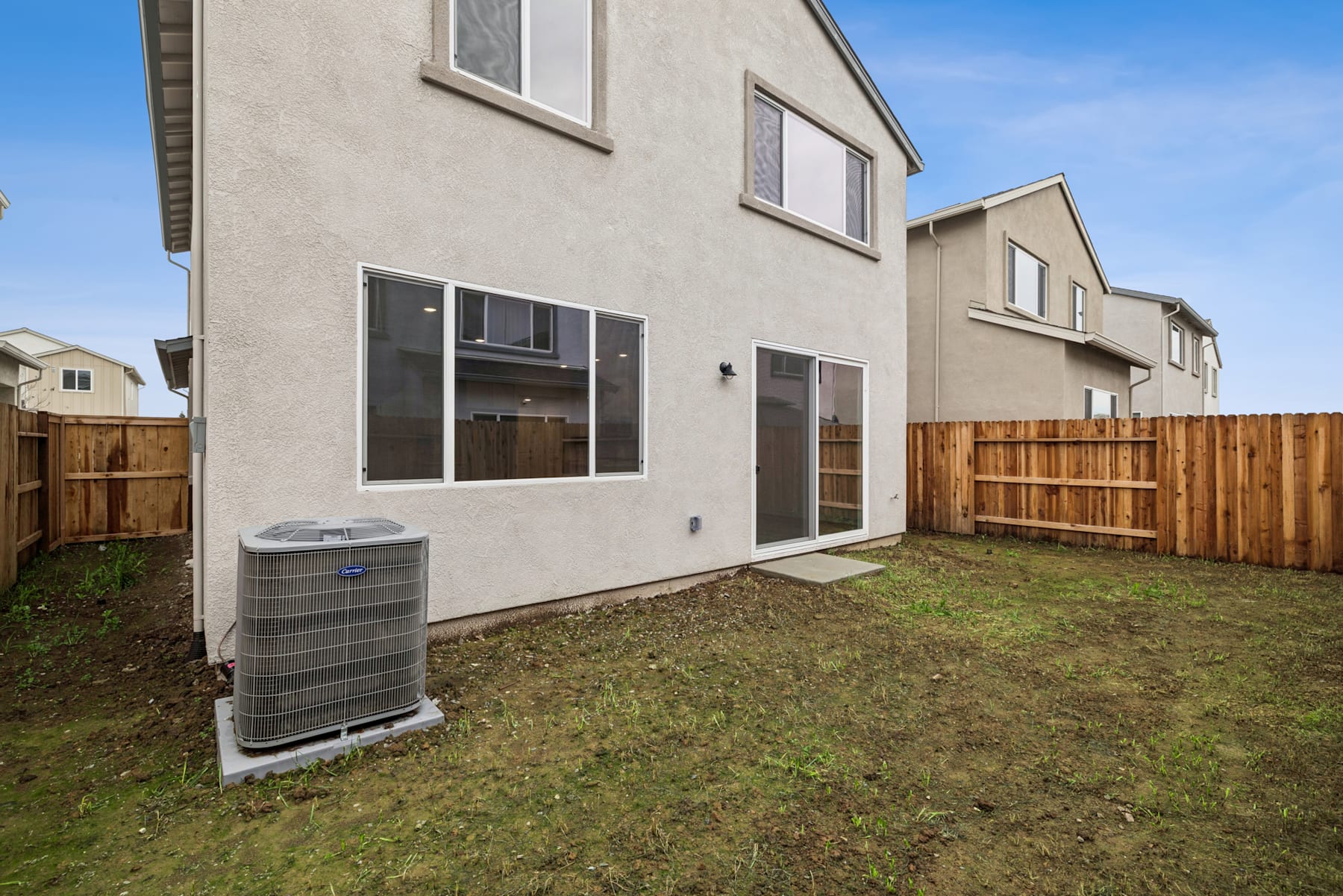 The image shows a residential townhouse with a fenced backyard, a central air conditioning unit, and a grassy lawn in the foreground.