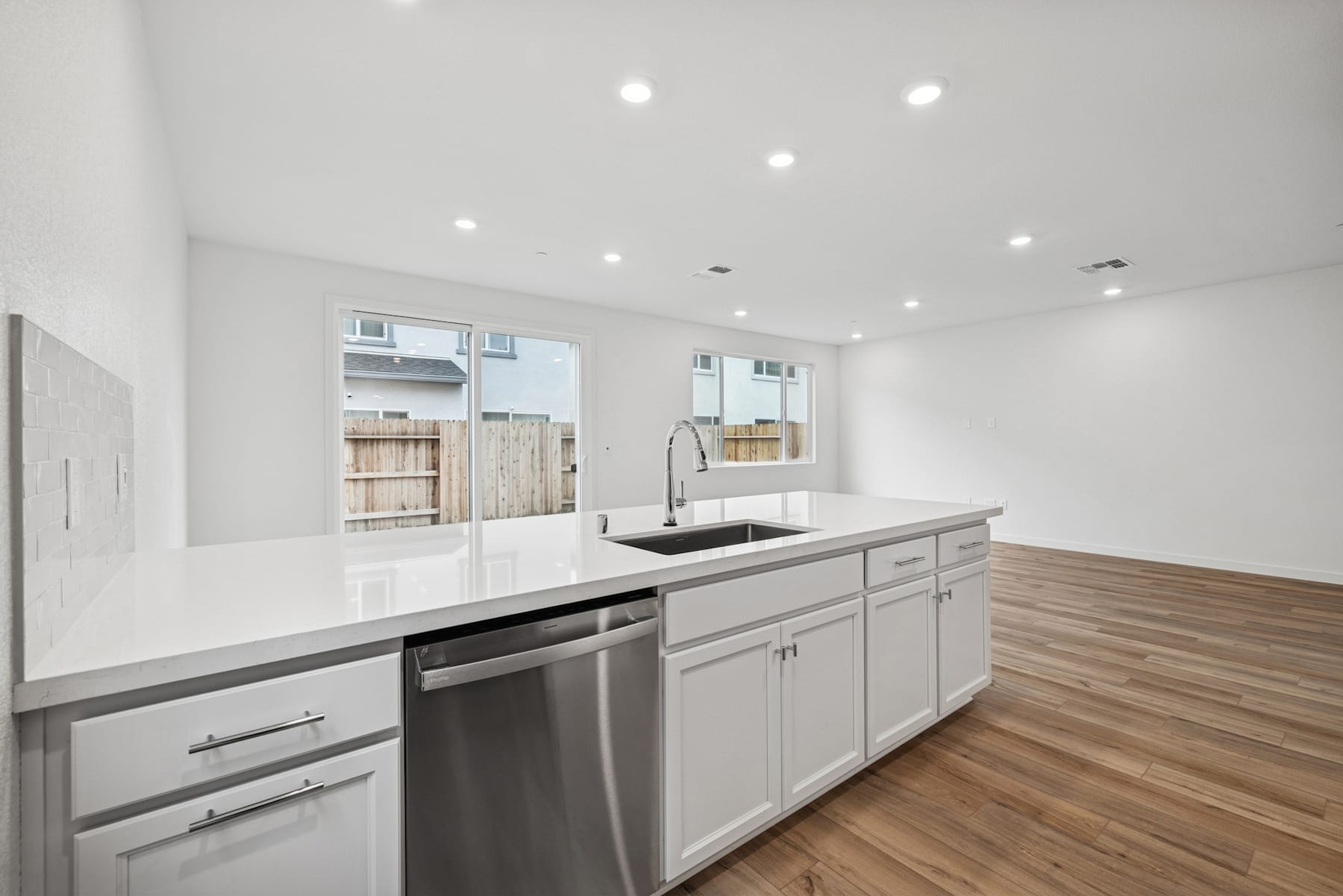 A modern, well-lit kitchen with white cabinets, stainless steel appliances, and a wooden floor.