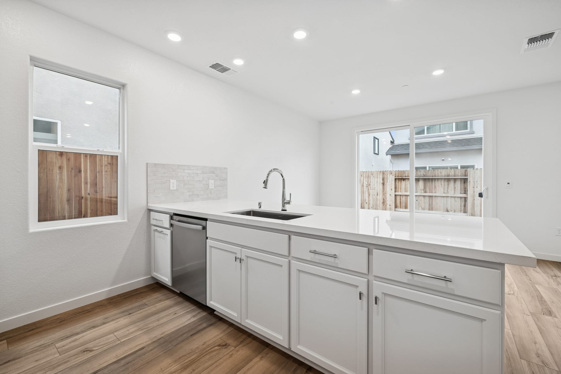 A modern, minimalist kitchen with white cabinets, stainless steel appliances, and a wooden floor.