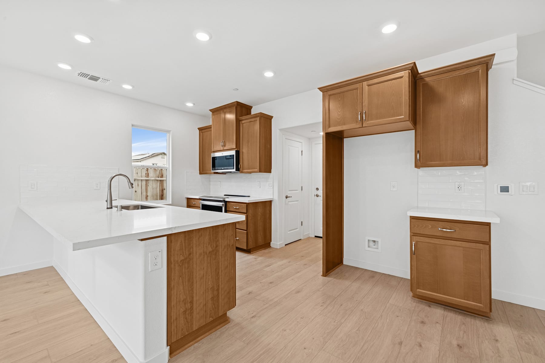 A modern, well-lit kitchen with wooden cabinets, a white countertop, and a hardwood floor.