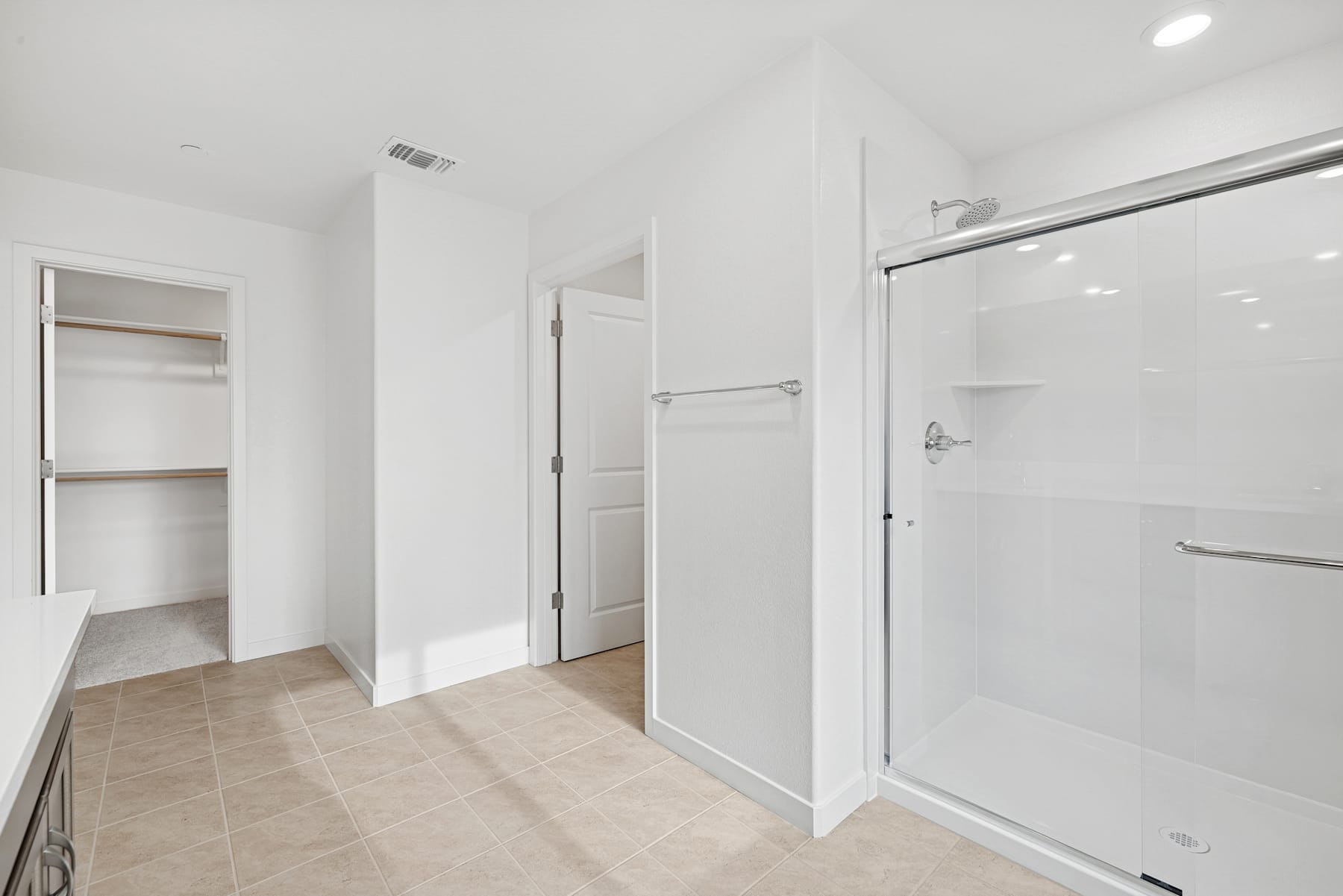 A bright, minimalist bathroom with a glass-enclosed shower, white walls, and a tiled floor.