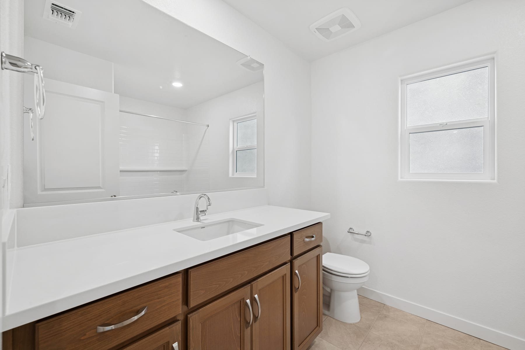 A modern, minimalist bathroom with a wooden vanity, a white sink, and a toilet against a white wall background.