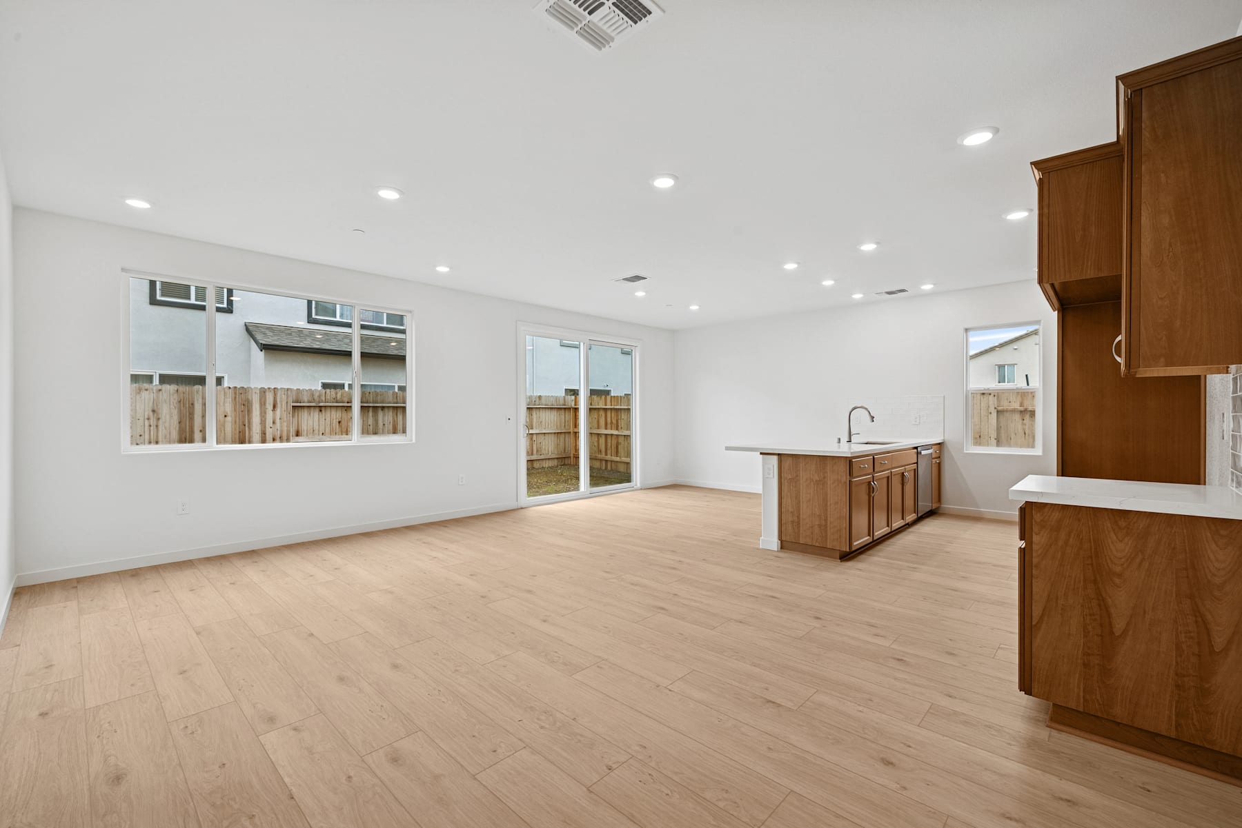 A spacious, open-concept living area with a wooden kitchen island, hardwood floors, and recessed lighting, overlooking a backyard through large windows.