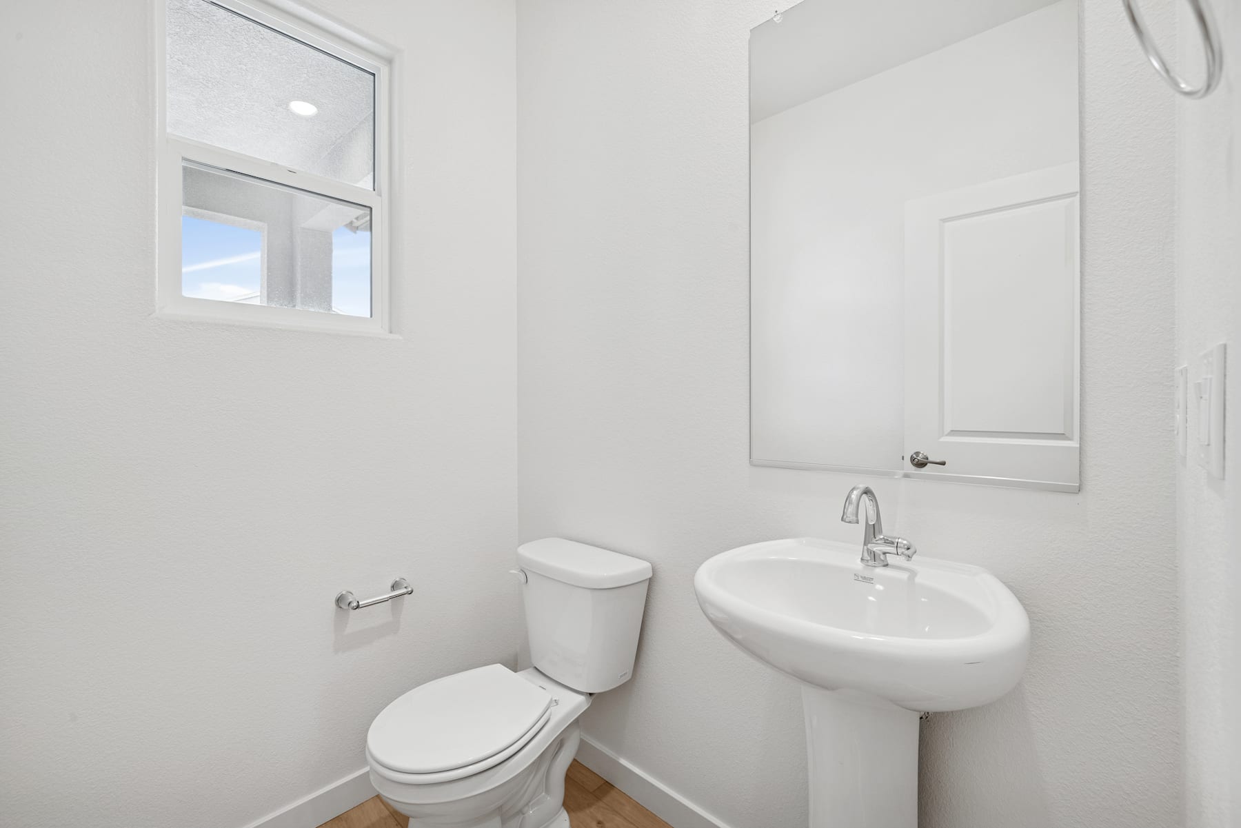A clean, minimalist bathroom with a white toilet, sink, and small window providing natural light.
