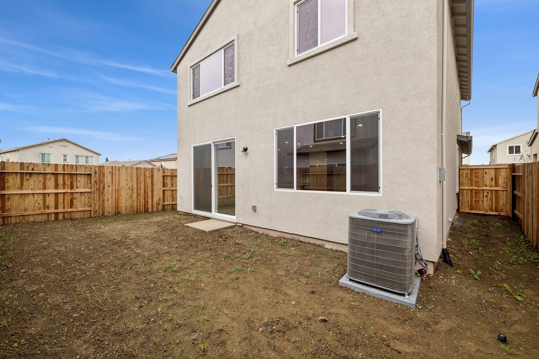 A two-story residential building with a fenced backyard and an air conditioning unit on the ground.