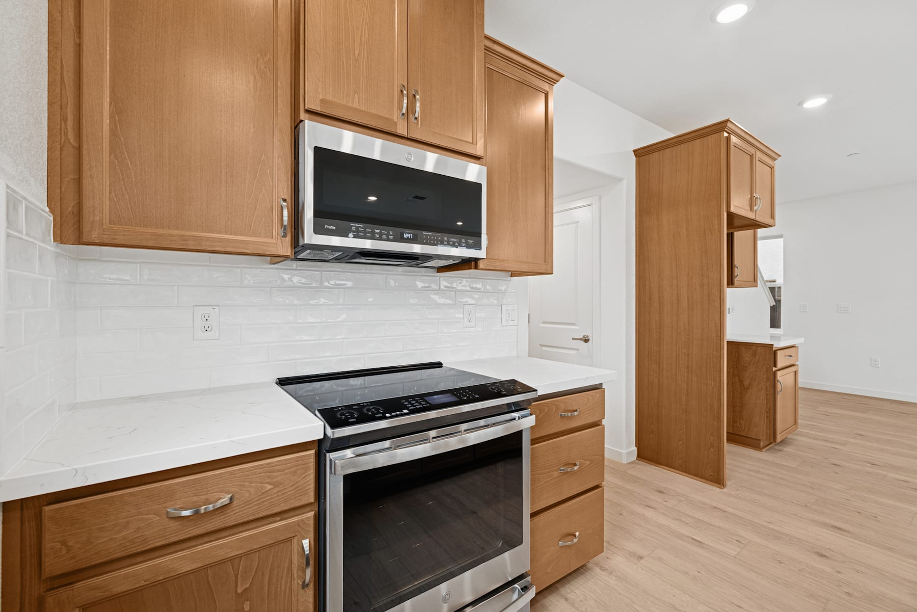 A modern kitchen with light wood cabinets, a stainless steel oven, and a microwave mounted above the oven.