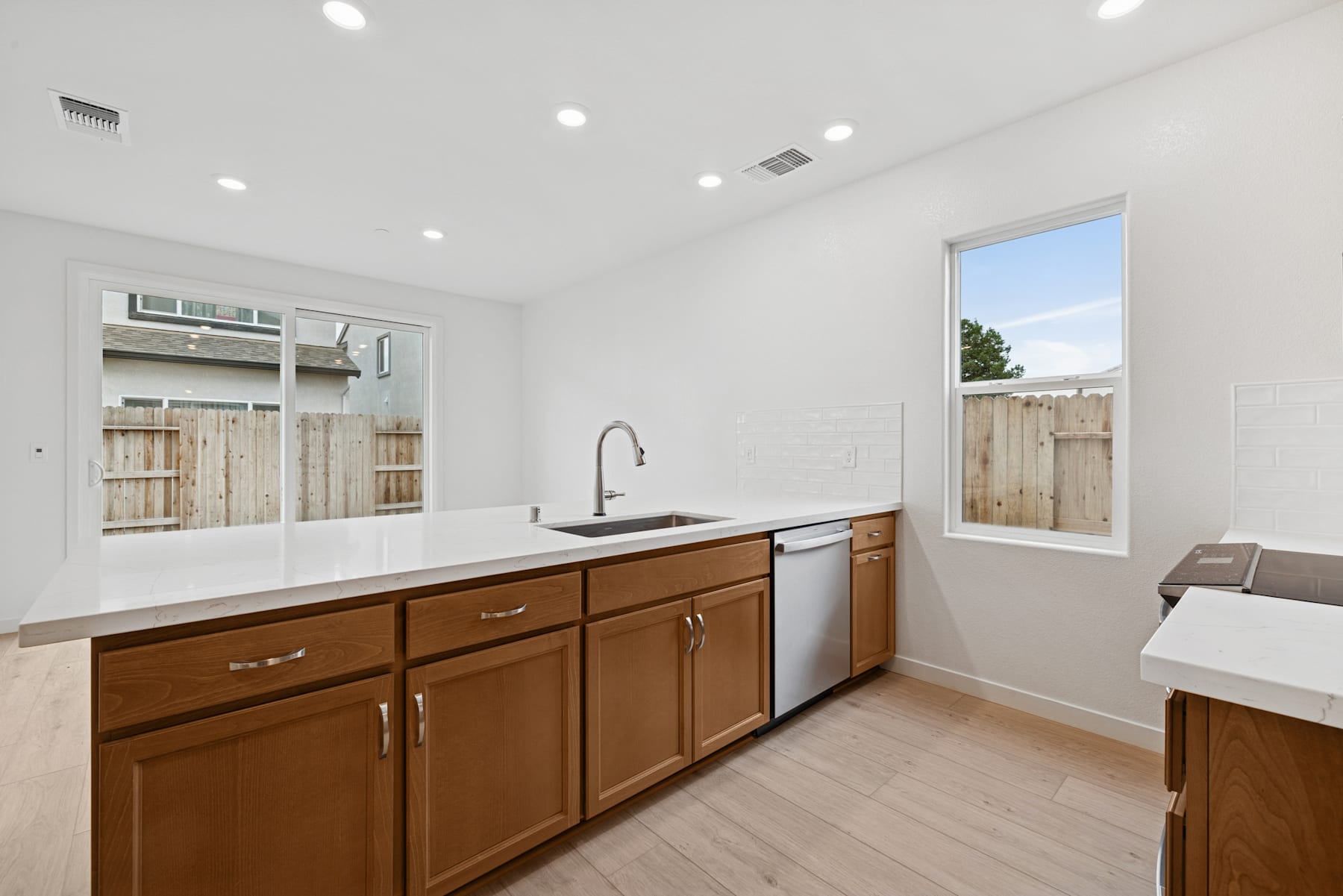 A modern, well-lit kitchen with wooden cabinets, a sink, and a window overlooking a backyard.