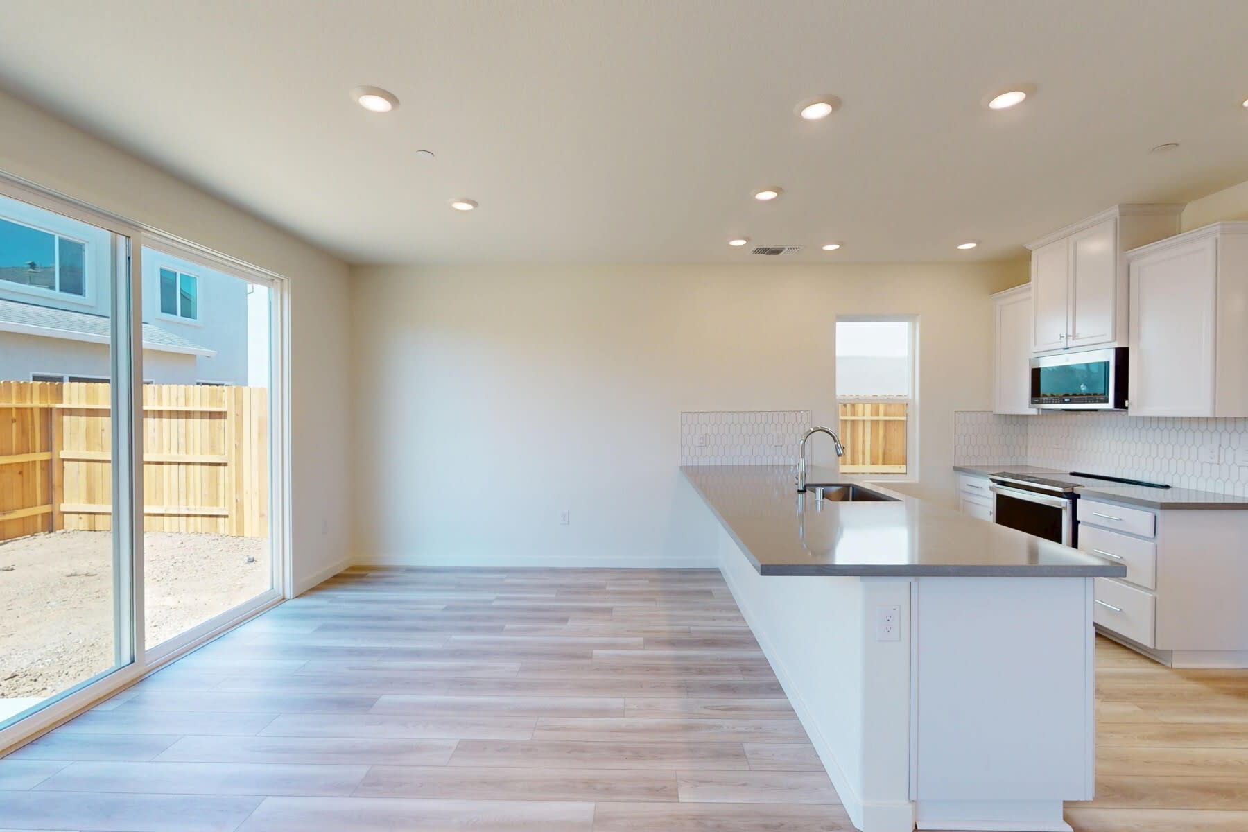 A modern, open-concept kitchen with white cabinets, a gray countertop, and a sliding glass door leading to an outdoor area.