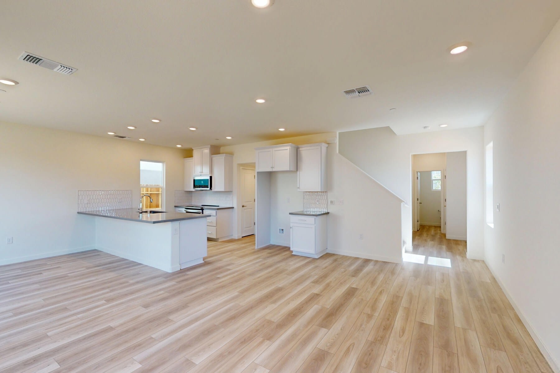 A modern, open-concept kitchen and living space with light-colored hardwood floors, white cabinets, and recessed lighting.