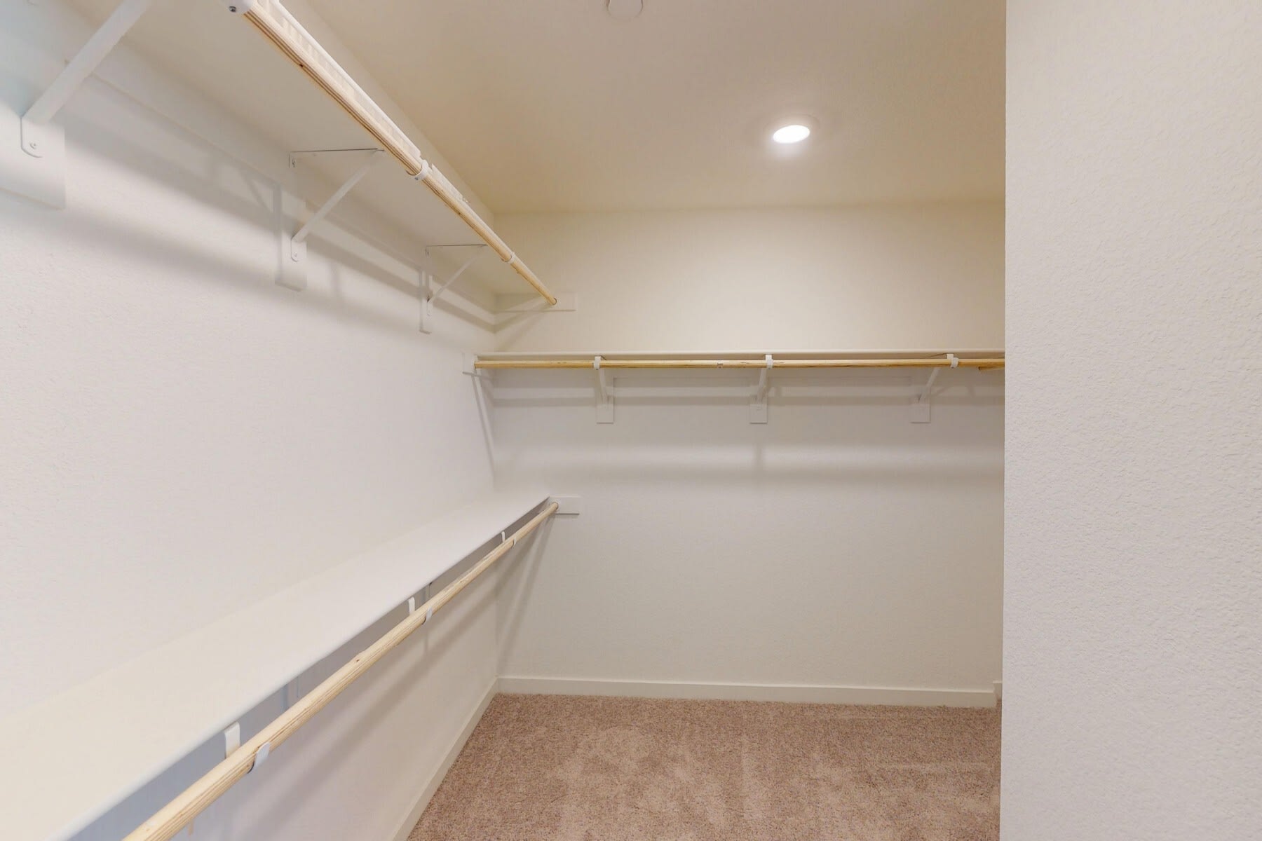 A spacious walk-in closet with ample shelving and hanging space, featuring a neutral color scheme and recessed lighting.