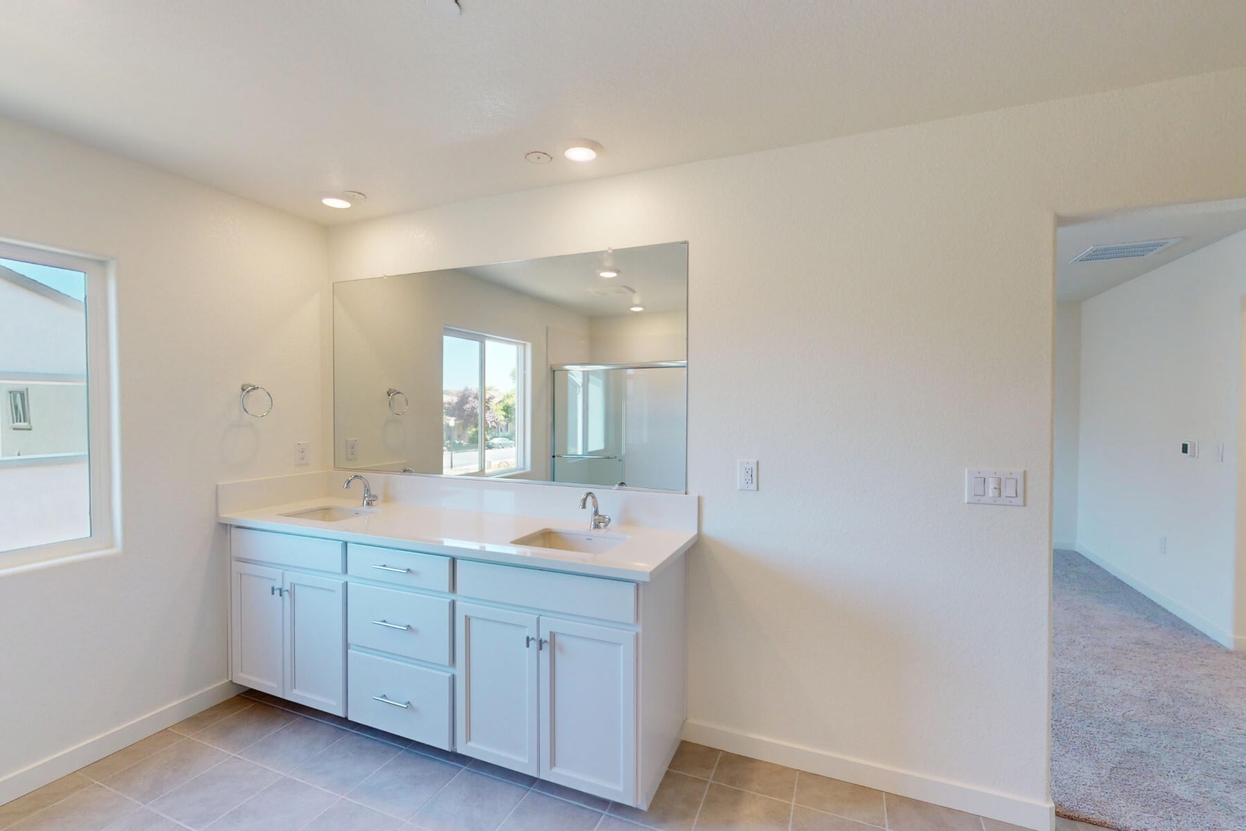 A modern bathroom vanity with a large mirror, recessed lighting, and a tiled floor in a bright, open room.