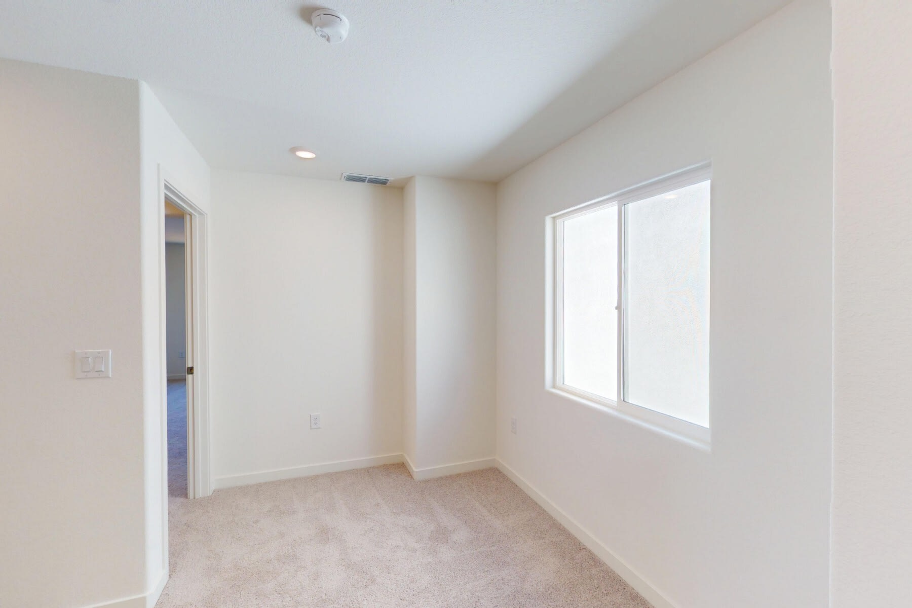 A simple, minimalist room with white walls, a window, and a door visible in the background.