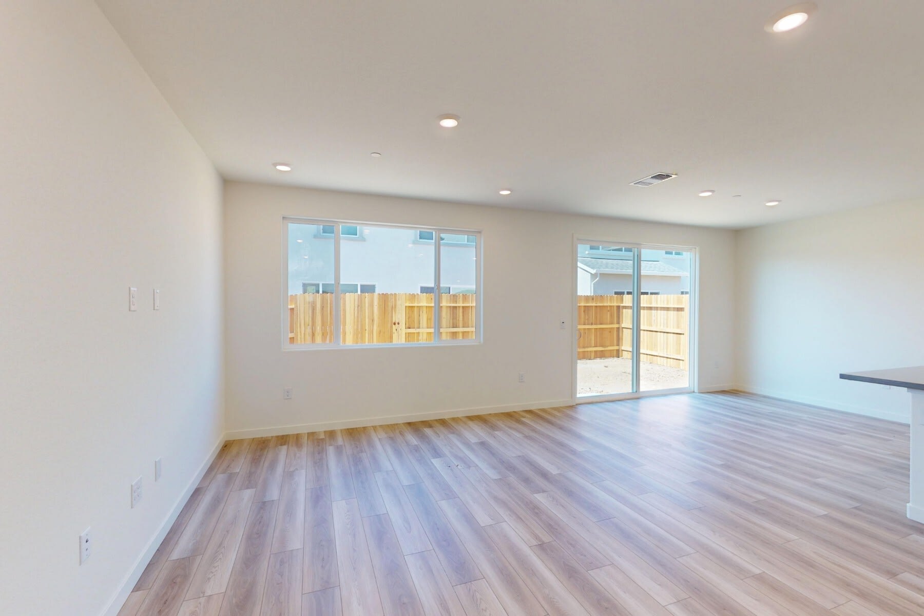 An empty, spacious room with white walls, a wooden floor, and a sliding glass door leading to an outdoor area.