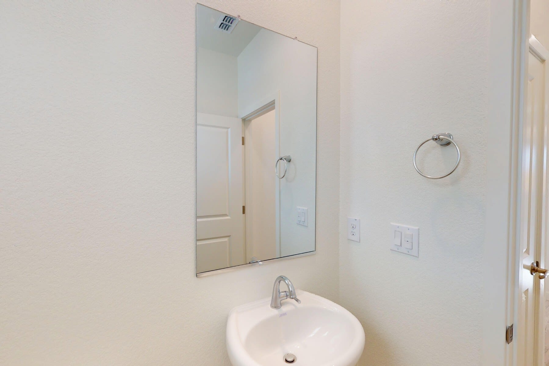A simple and clean bathroom with a white sink, mirror, and towel ring on the wall.