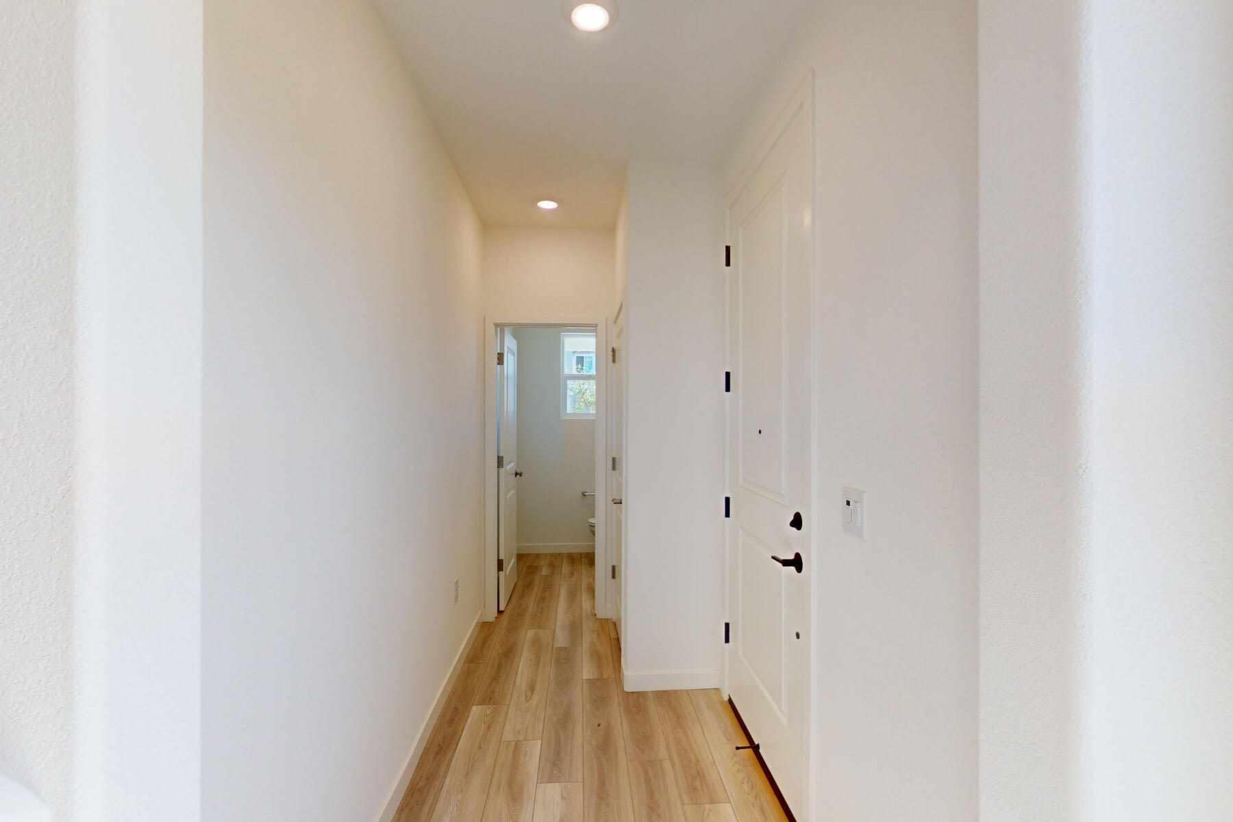 A well-lit, minimalist hallway with white walls, a wooden floor, and several doors leading to other rooms.