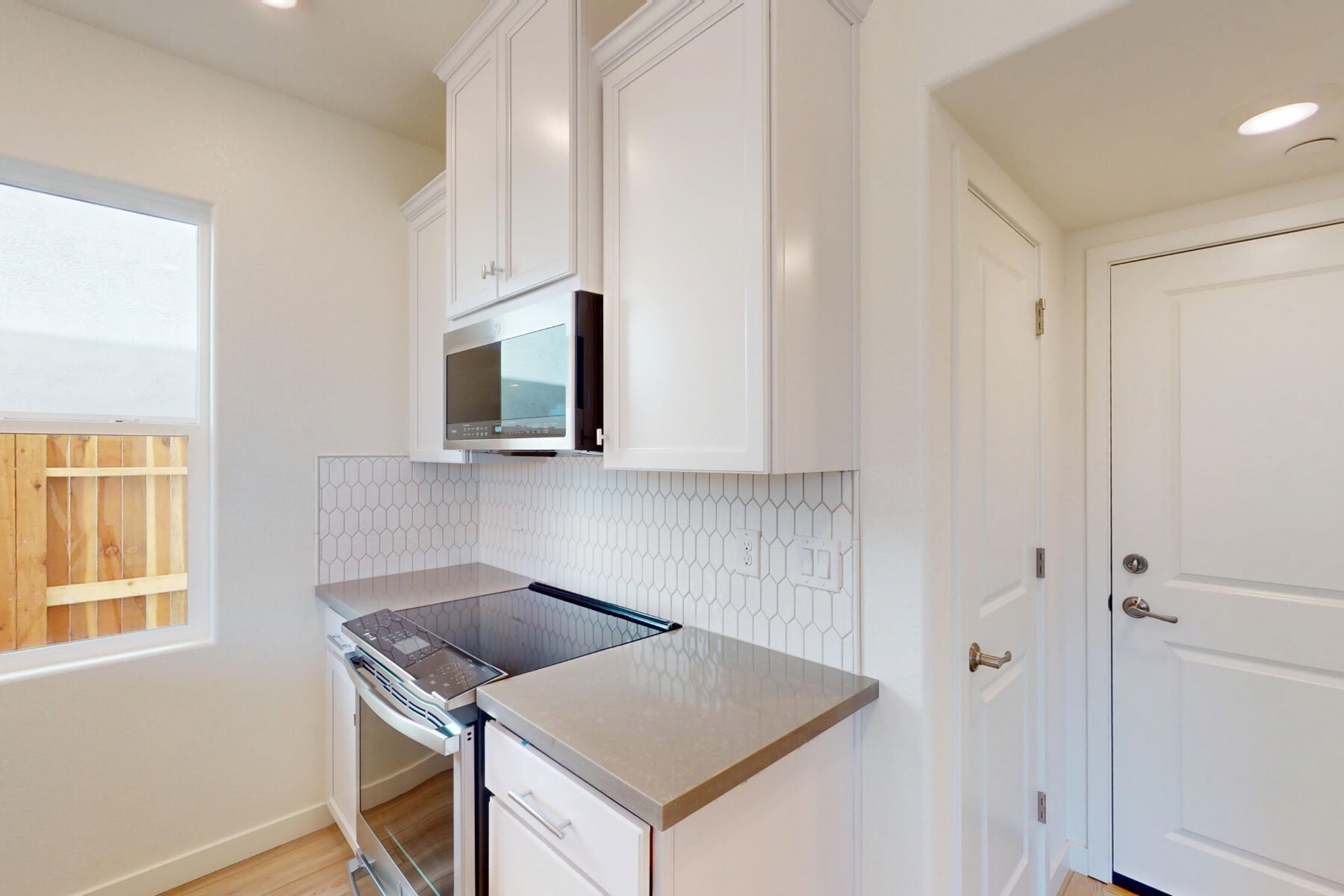 A modern, minimalist kitchen with white cabinets, a stainless steel appliance, and a tiled backsplash, set against a bright and airy background.