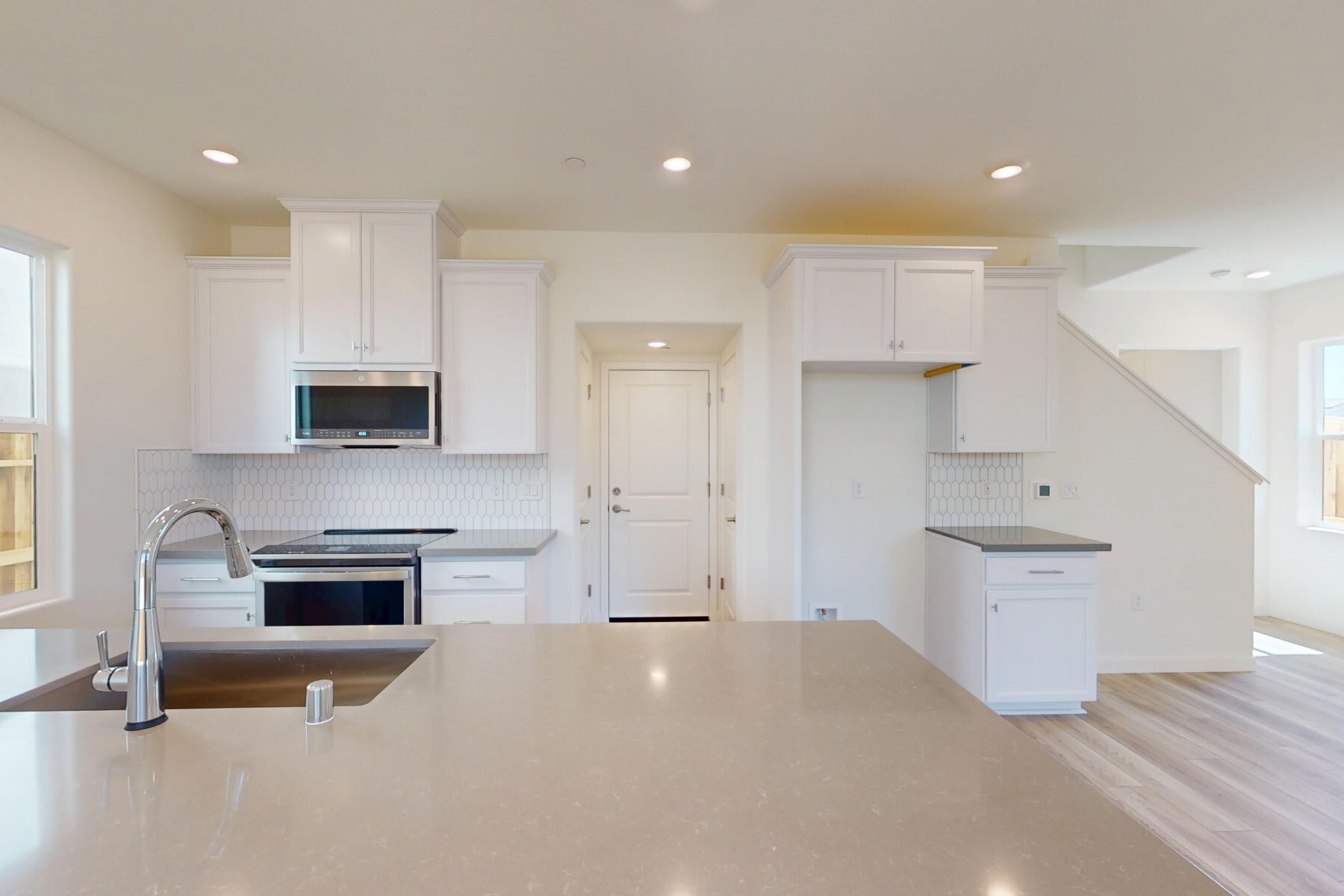 A bright and spacious kitchen with white cabinets, stainless steel appliances, and a large countertop island in the foreground.