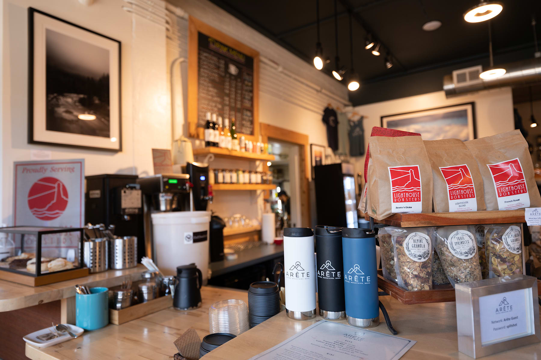 A cozy coffee shop interior with various coffee-related products and equipment displayed on the counter, including bags of coffee beans, mugs, and other accessories.