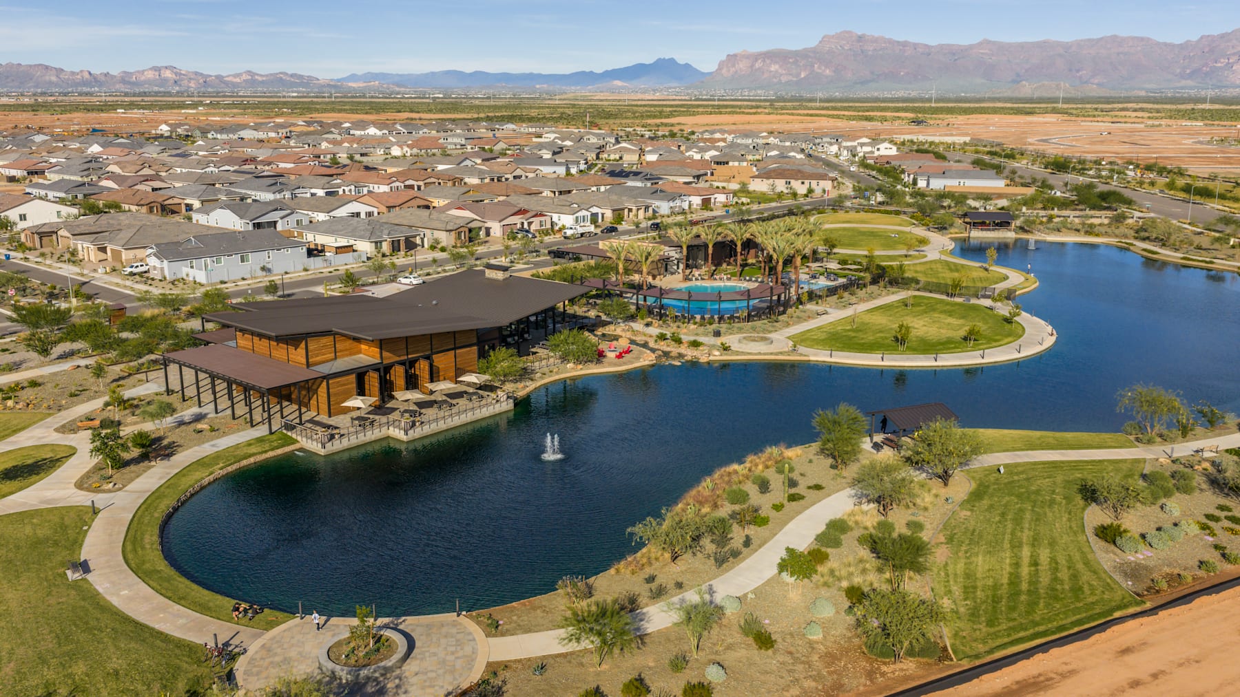 A sprawling residential community nestled among lush green landscapes, with a central lake and recreational facilities, surrounded by majestic mountains in the distance.