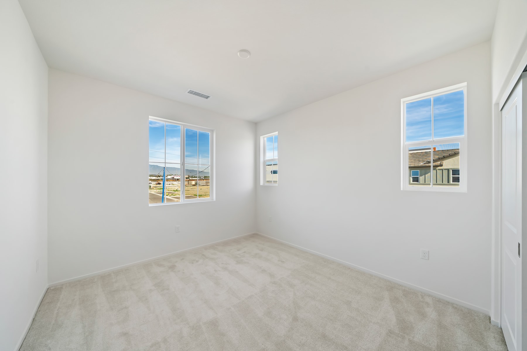 A bright, empty room with white walls, hardwood floors, and large windows providing a view of the exterior.