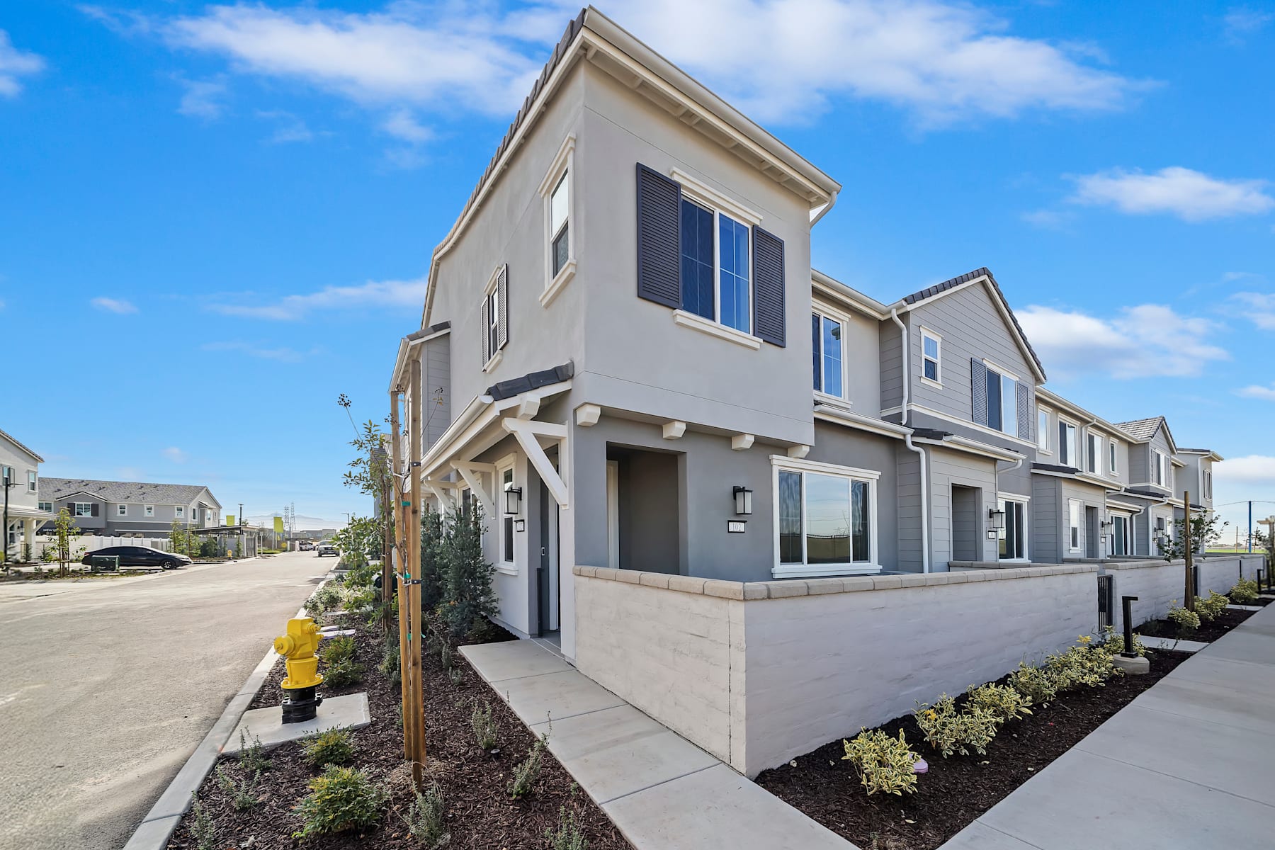 A modern, multi-story townhouse complex with a well-landscaped front yard and a clear blue sky in the background.