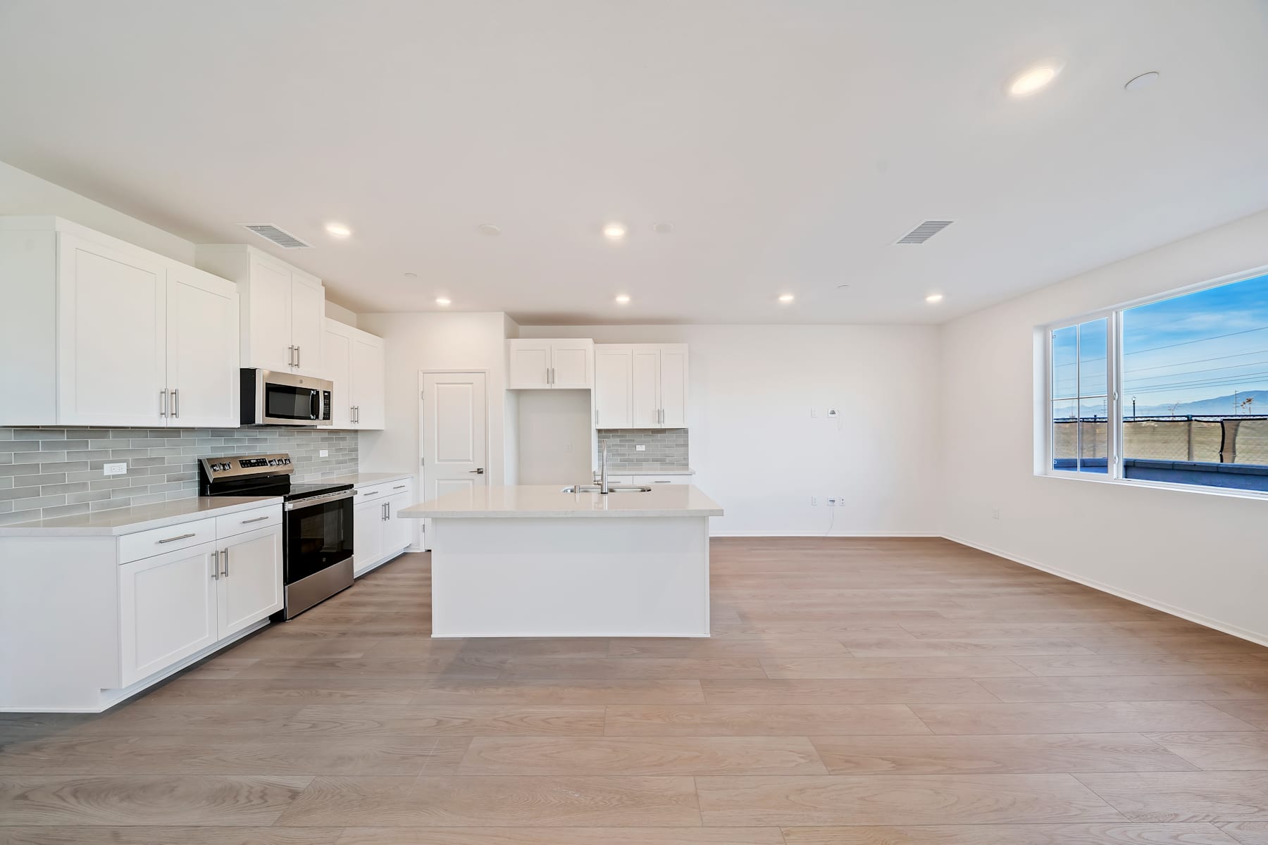 A modern, open-concept kitchen with white cabinets, stainless steel appliances, and a large window overlooking a scenic outdoor view.