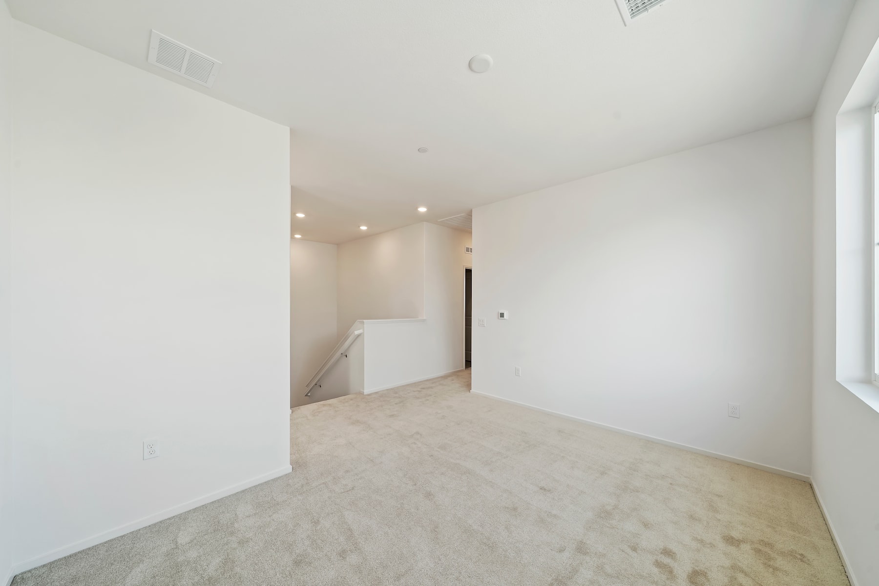 A spacious, minimalist room with white walls, a light-colored floor, and a doorway visible in the background.