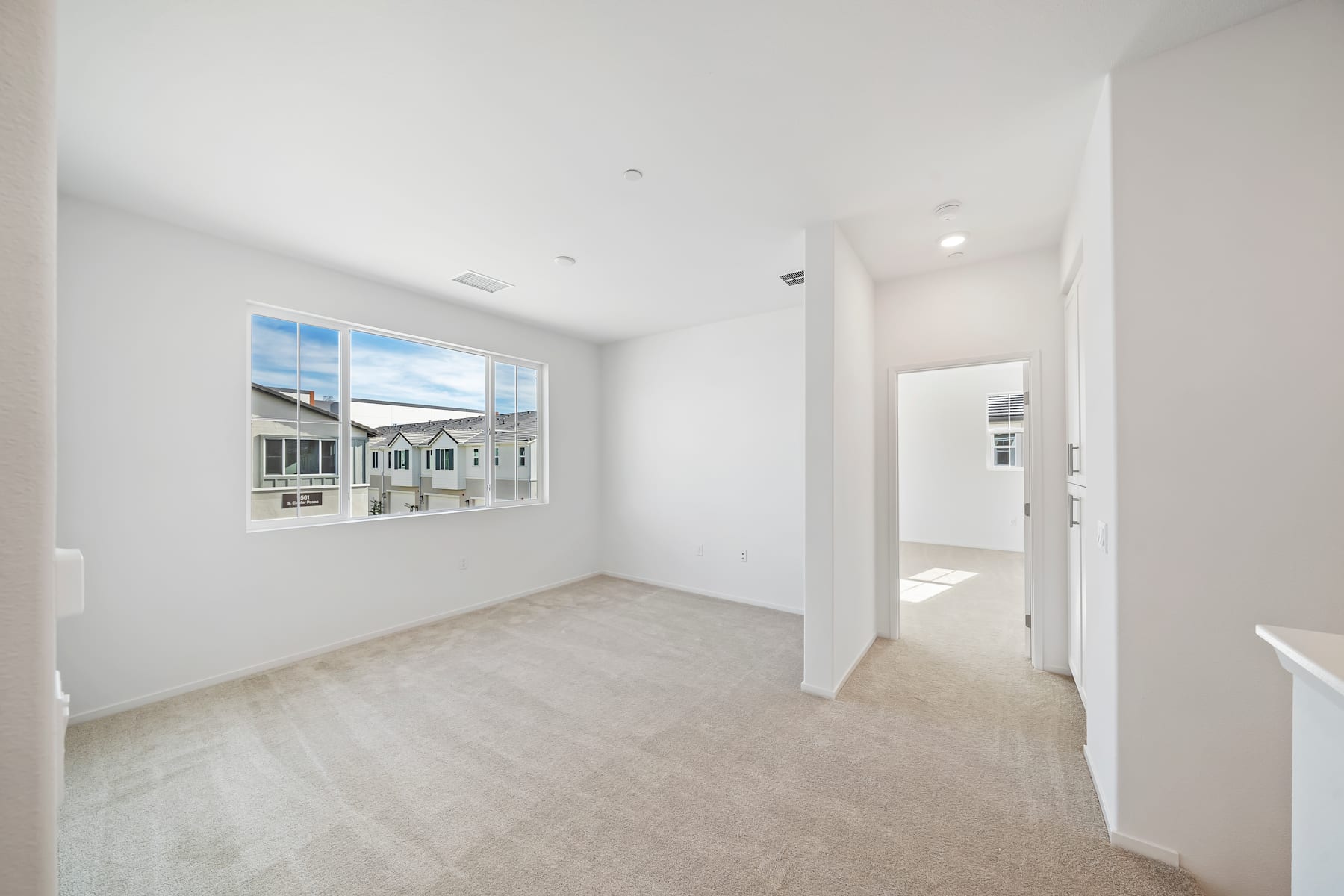 A bright and spacious room with a large window overlooking a residential neighborhood, featuring hardwood floors and a clean, minimalist design.