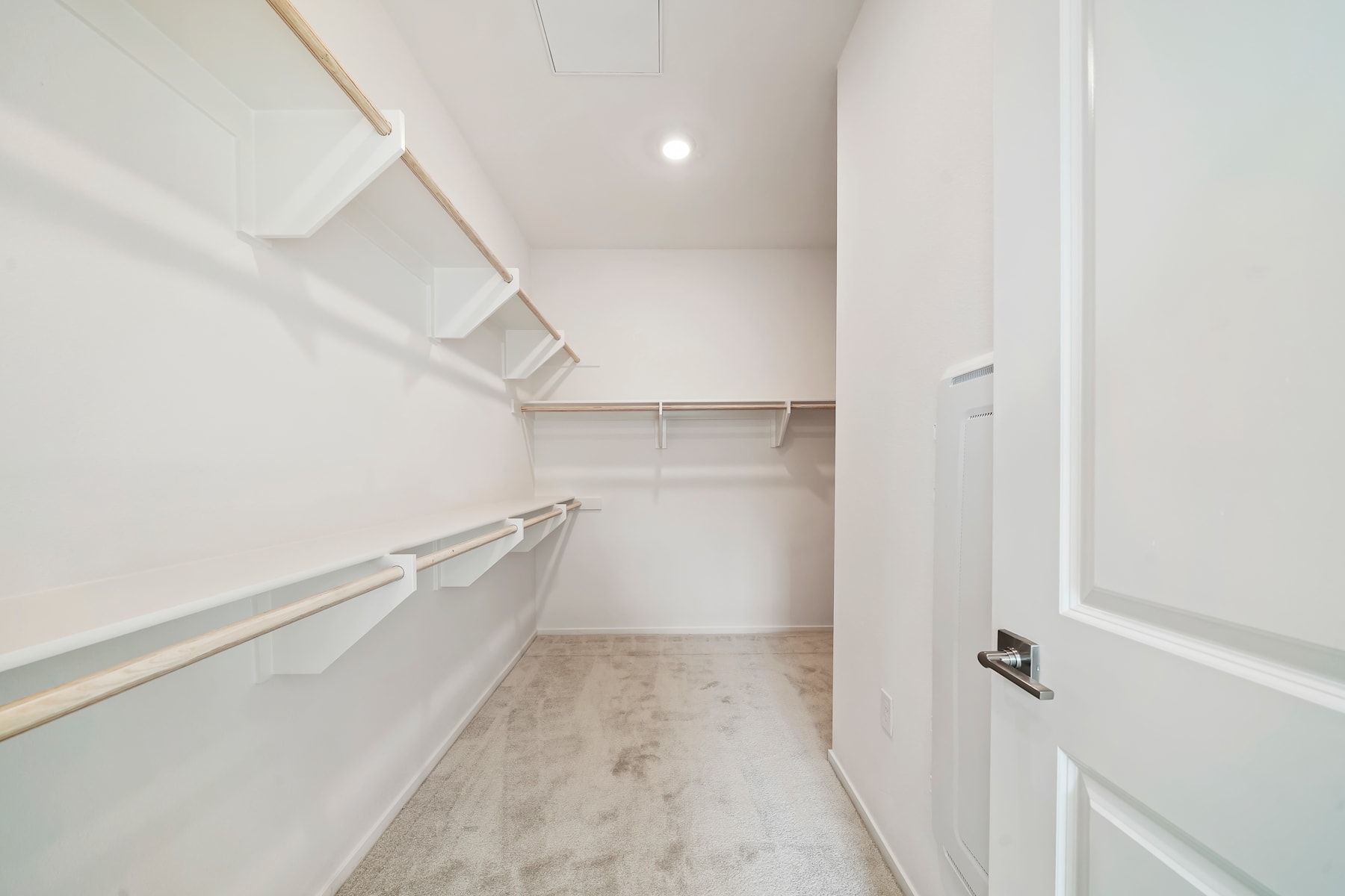 A bright, minimalist walk-in closet with white walls, shelves, and a tiled floor.