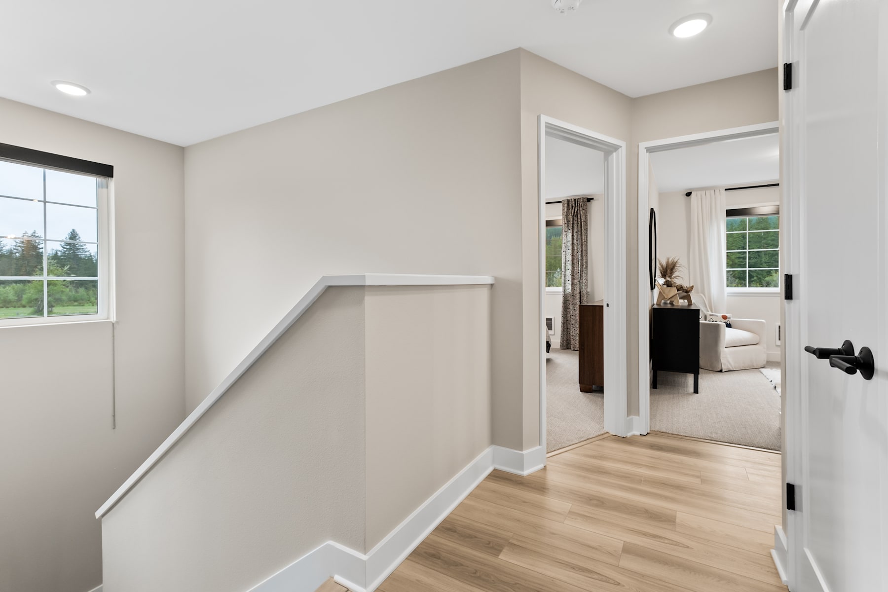 A spacious and well-lit hallway with a wooden floor, leading to an open doorway that reveals a bedroom in the background.