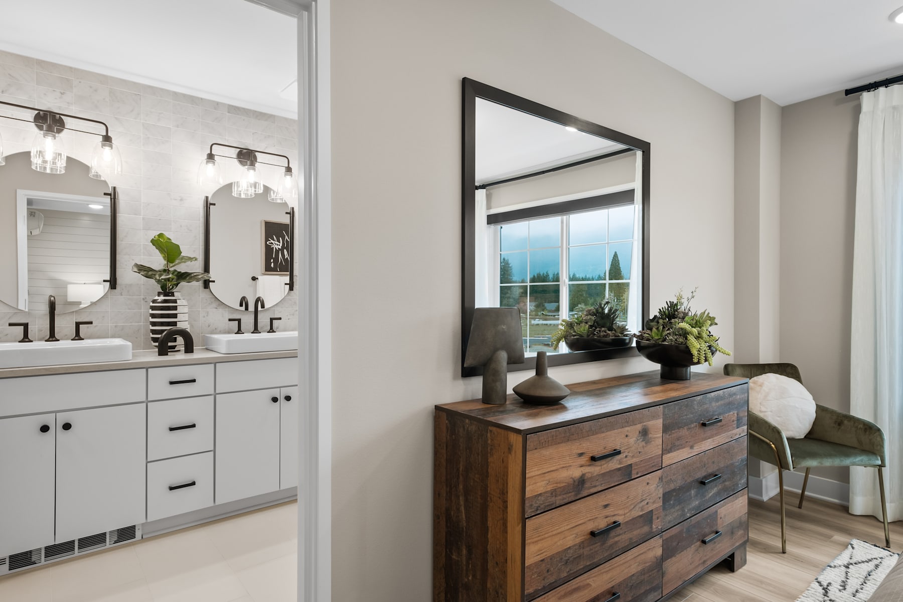 A modern and stylish bathroom with a large mirror, vanity, and decorative elements such as plants and a wooden dresser in the background.