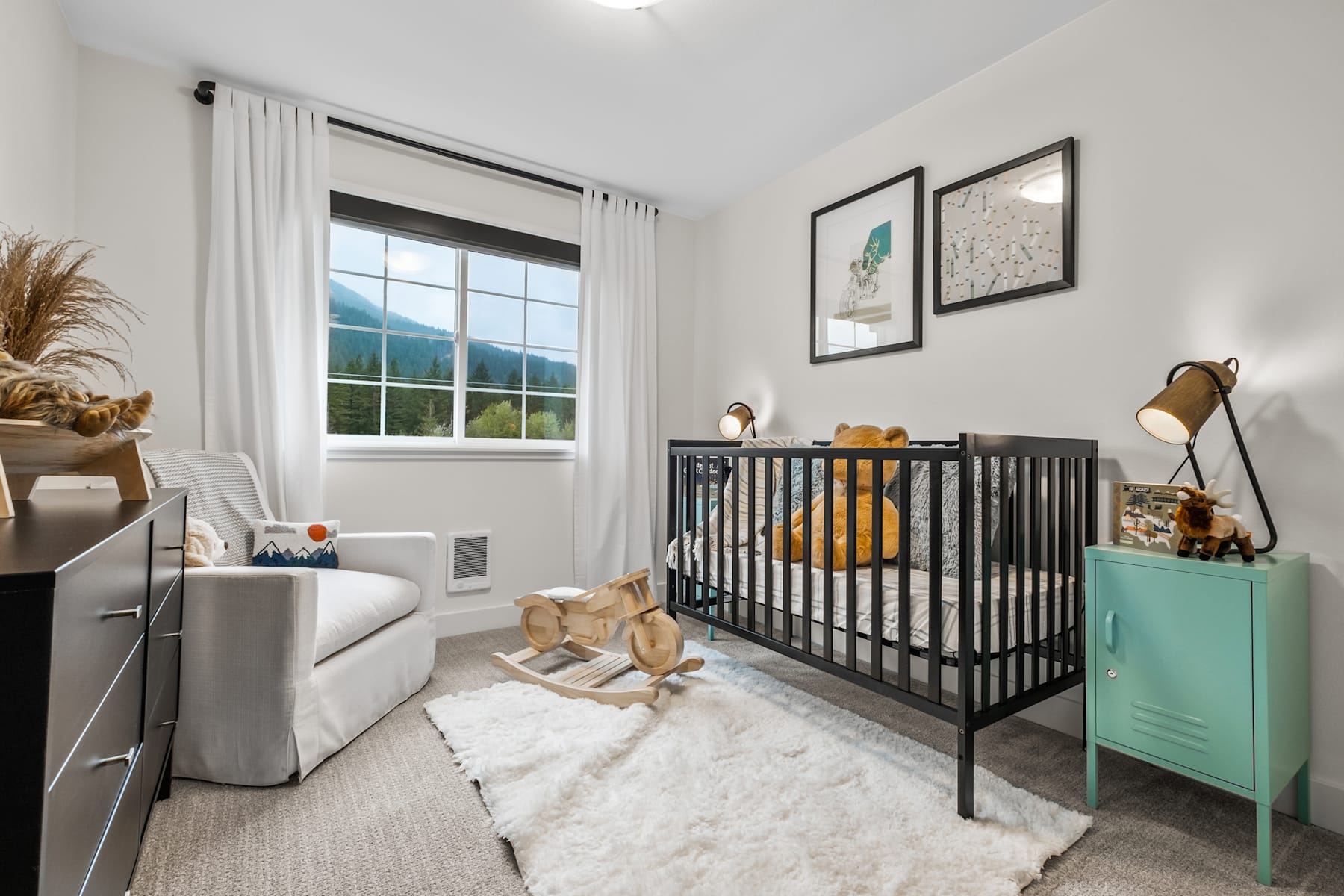 A cozy and well-appointed nursery with a black crib, a comfortable armchair, and a scenic window overlooking a natural landscape.
