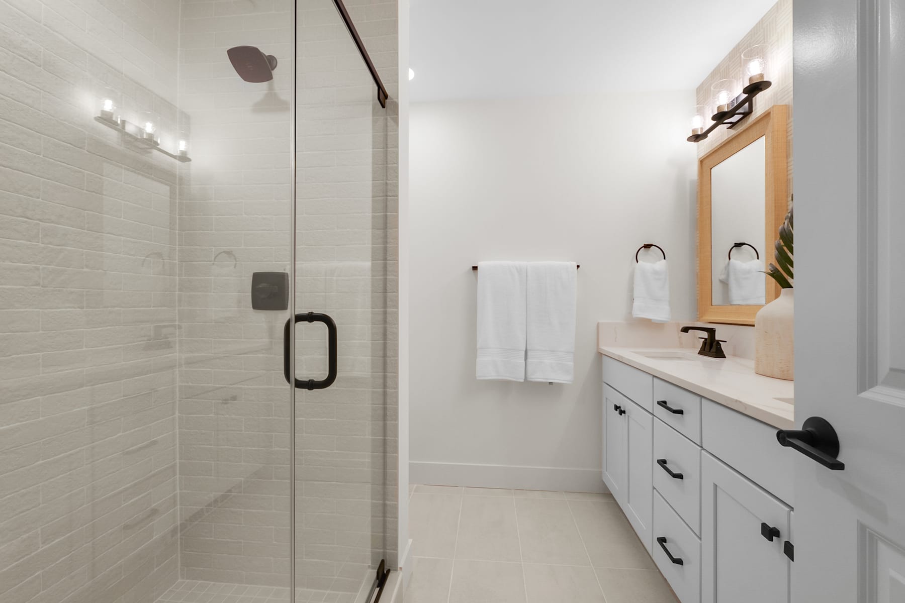 A modern, well-lit bathroom with a glass-enclosed shower, a white vanity with drawers, and a framed mirror on the wall.