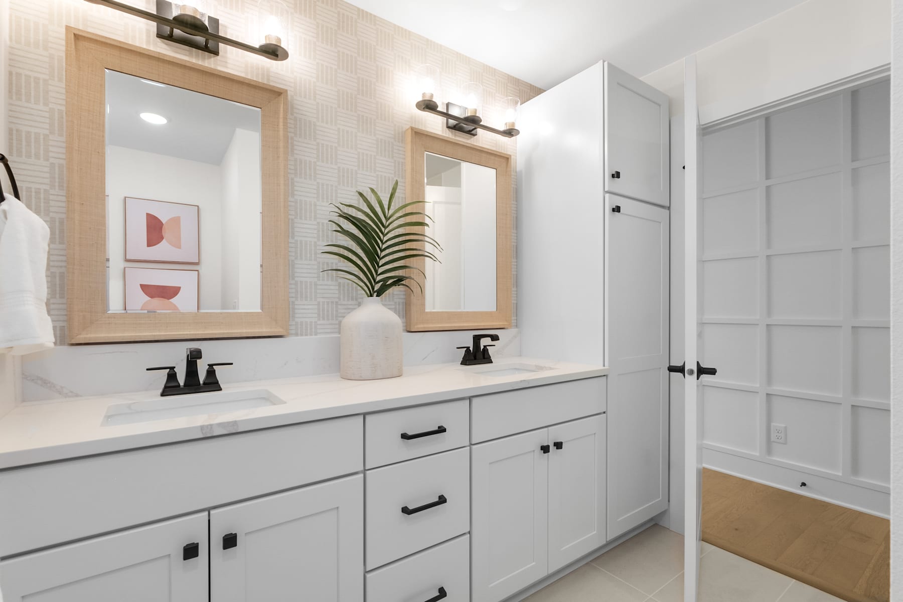 A modern and minimalist bathroom with a white vanity, framed mirrors, and a potted plant, creating a clean and serene atmosphere.