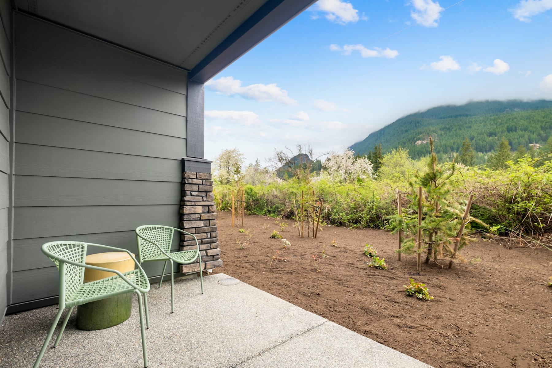A cozy outdoor seating area with green chairs overlooking a lush, mountainous landscape with a cloudy blue sky.
