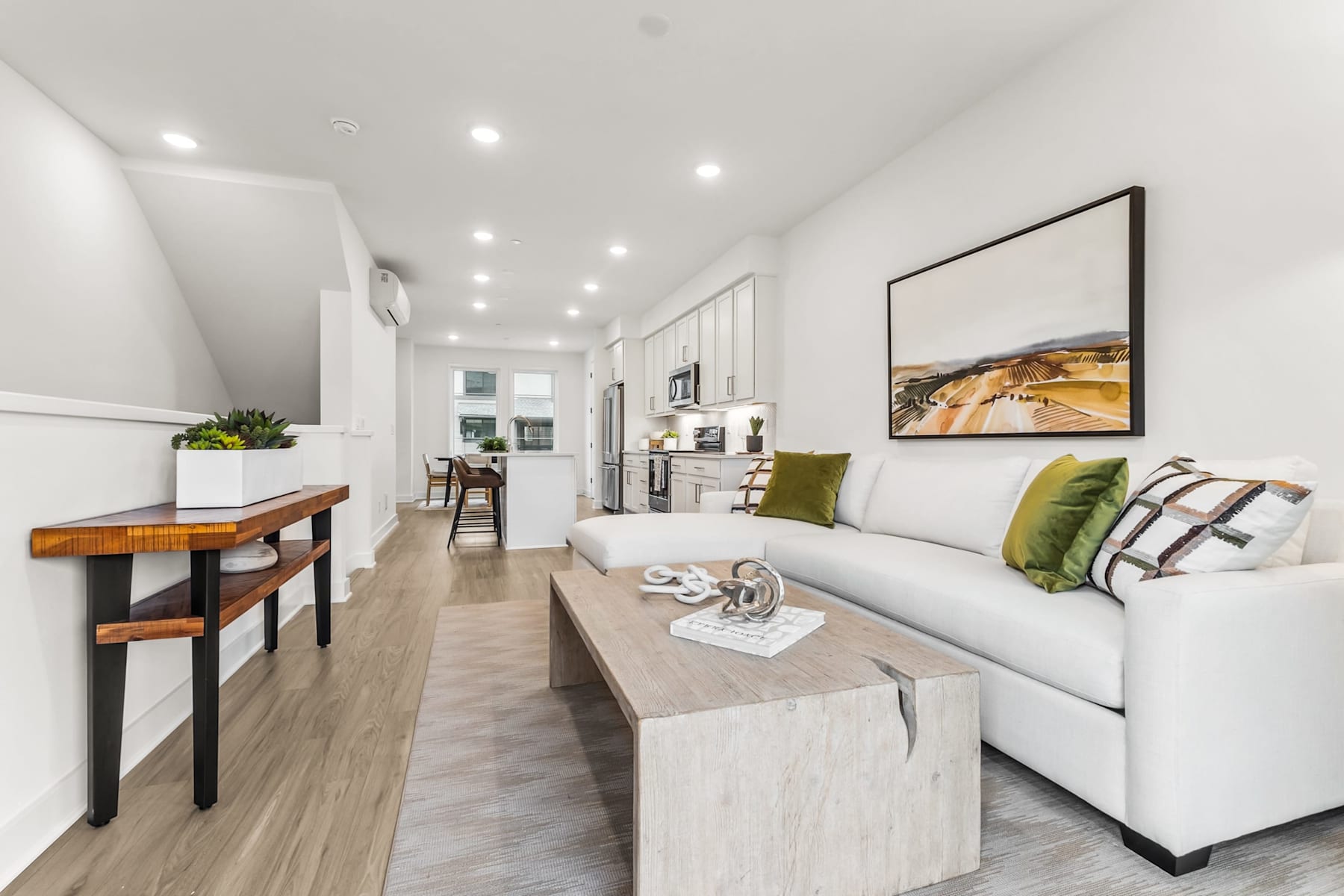 A modern and minimalist living room with a white sofa, wooden console table, and a framed landscape artwork on the wall.