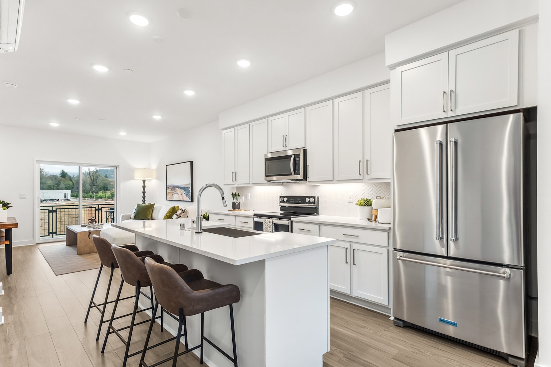 A modern, bright, and spacious kitchen with white cabinets, stainless steel appliances, and a large island with bar stools.