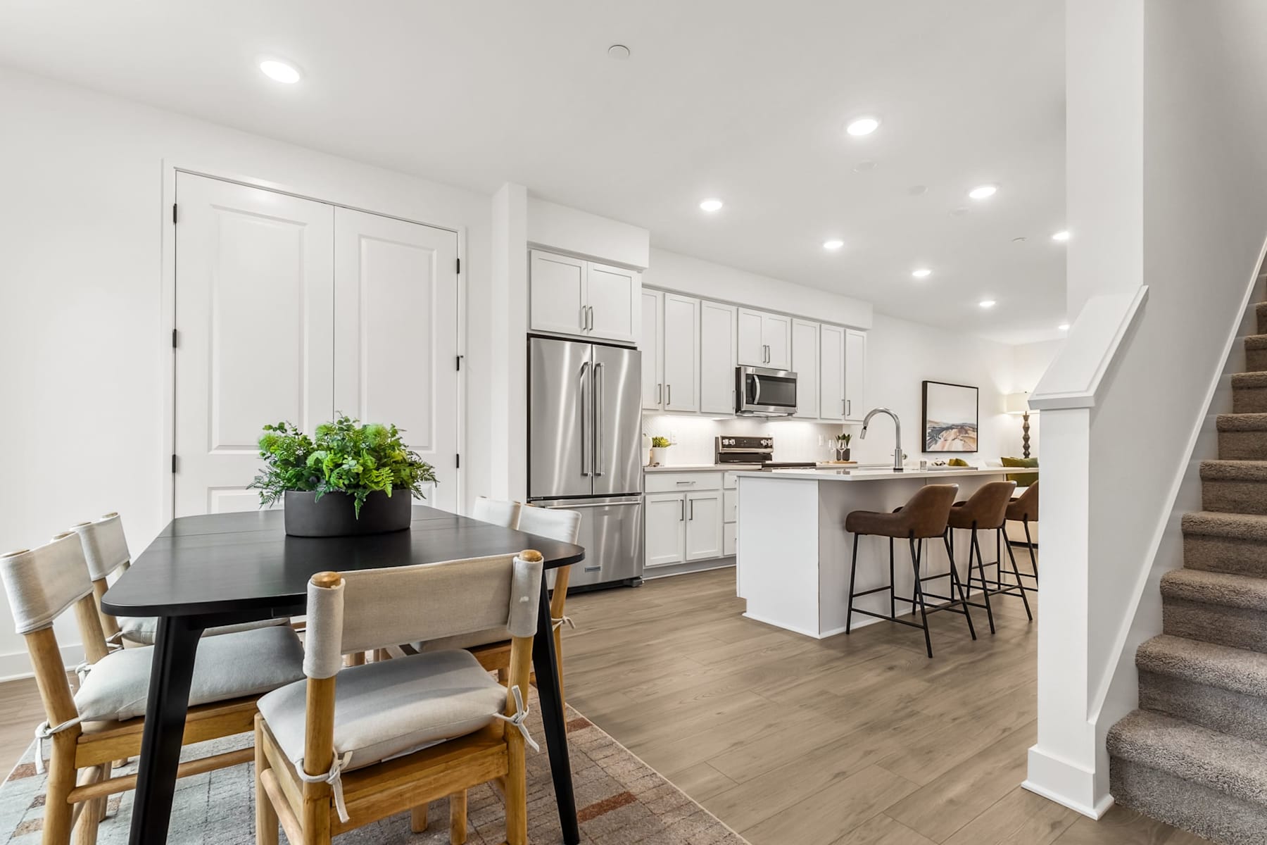 A modern, open-concept kitchen and dining area with white cabinets, stainless steel appliances, and a wooden dining table with chairs.