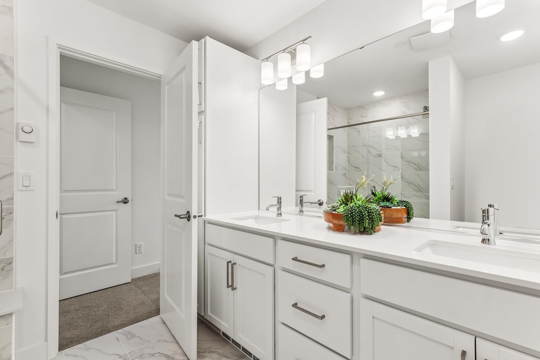 A modern, well-lit bathroom with white cabinets, a marble countertop, and a potted plant on the vanity.