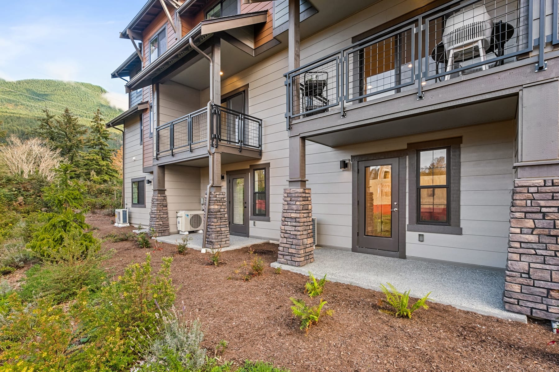 A multi-story residential building with balconies, surrounded by landscaped greenery and a mountainous backdrop.