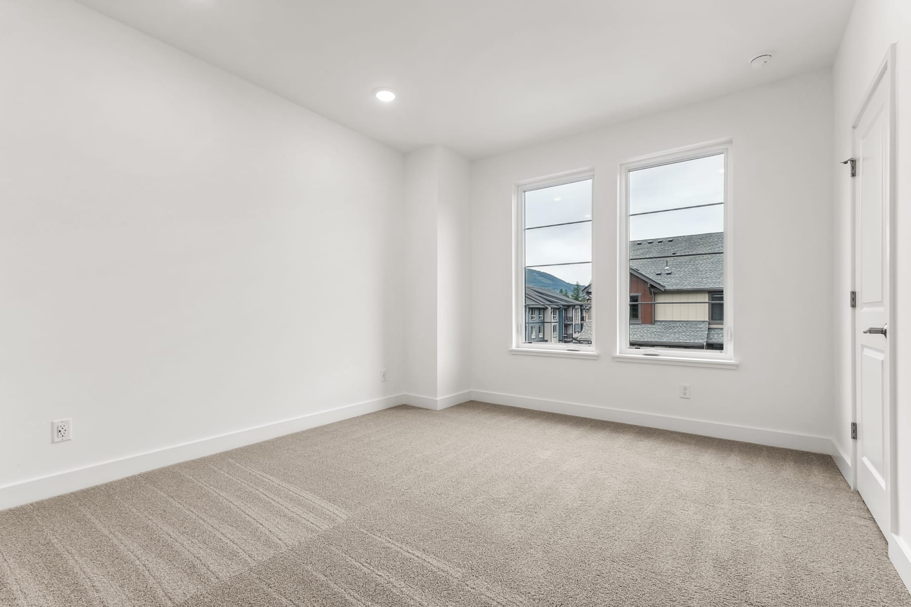A bright, spacious room with white walls, large windows, and a neutral-colored carpet covering the floor.