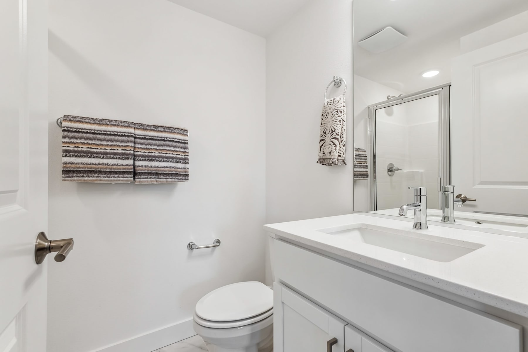 A modern, minimalist bathroom with a white vanity, a large mirror, and a striped towel rack on the wall.