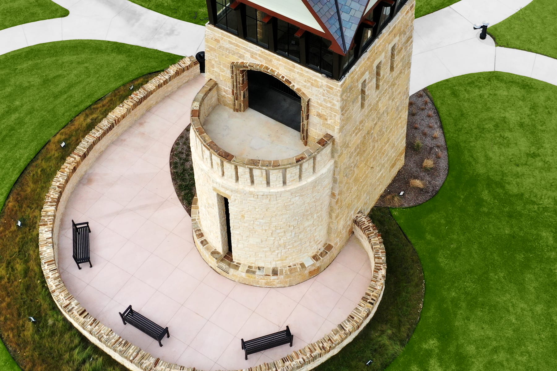 A stone tower stands on a grassy mound, surrounded by a circular path with benches, against a backdrop of lush green hills.