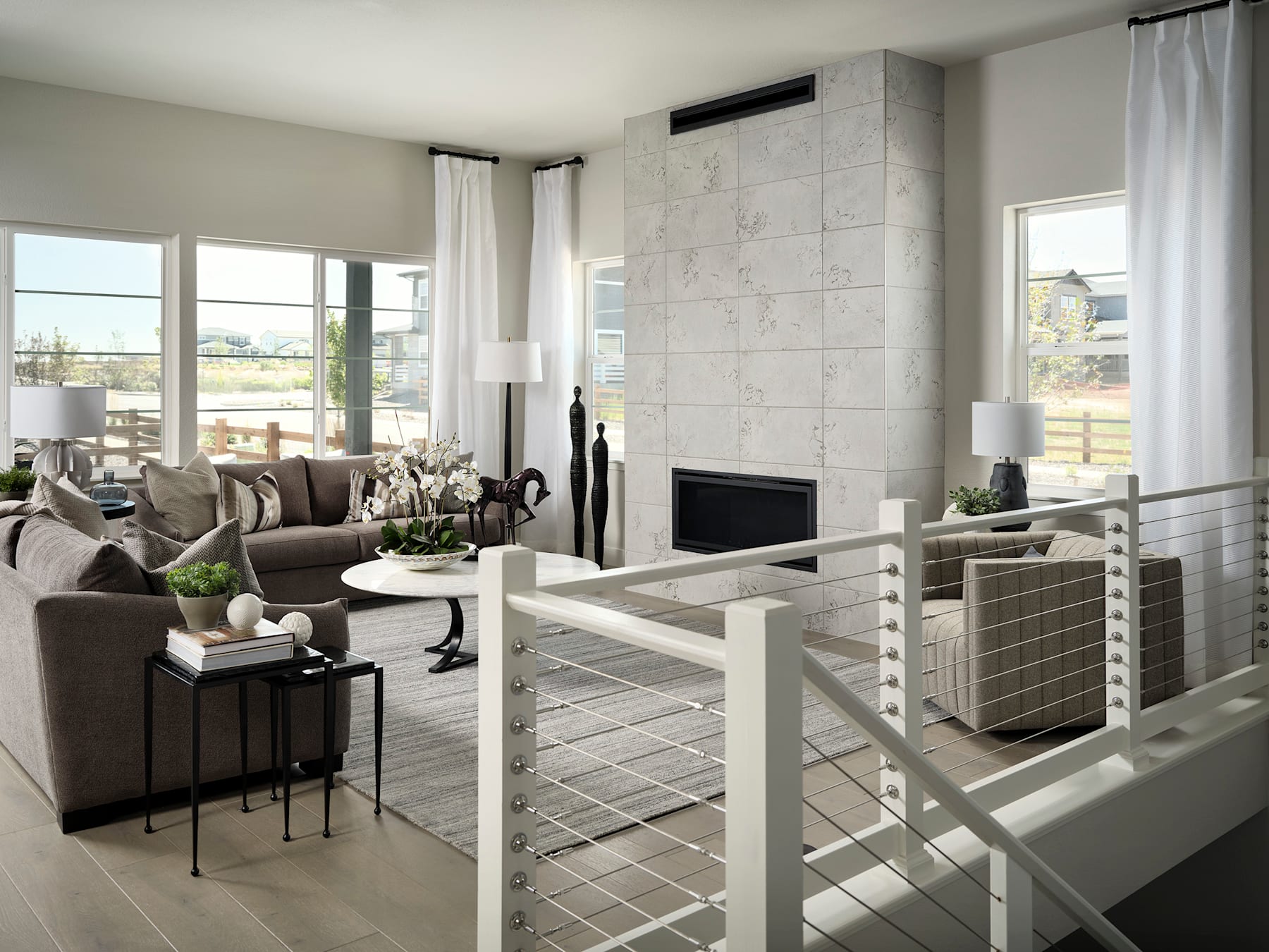 A modern and minimalist living room with a fireplace, large windows, and a mix of neutral-toned furniture and decor.