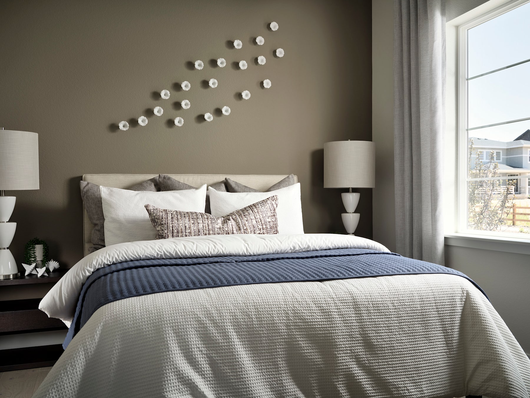 A cozy and inviting bedroom with a gray and white color scheme, featuring a plush bedding set, decorative wall accents, and a large window providing natural light.