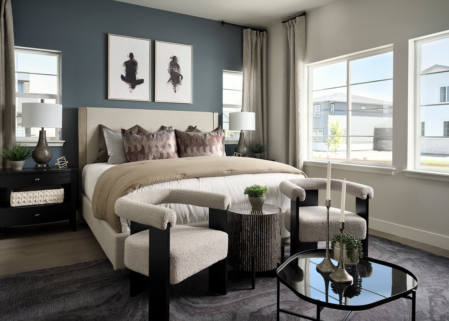 A cozy and stylish bedroom with a plush bed, decorative pillows, and framed artwork on the walls, set against a backdrop of large windows and a neutral color scheme.